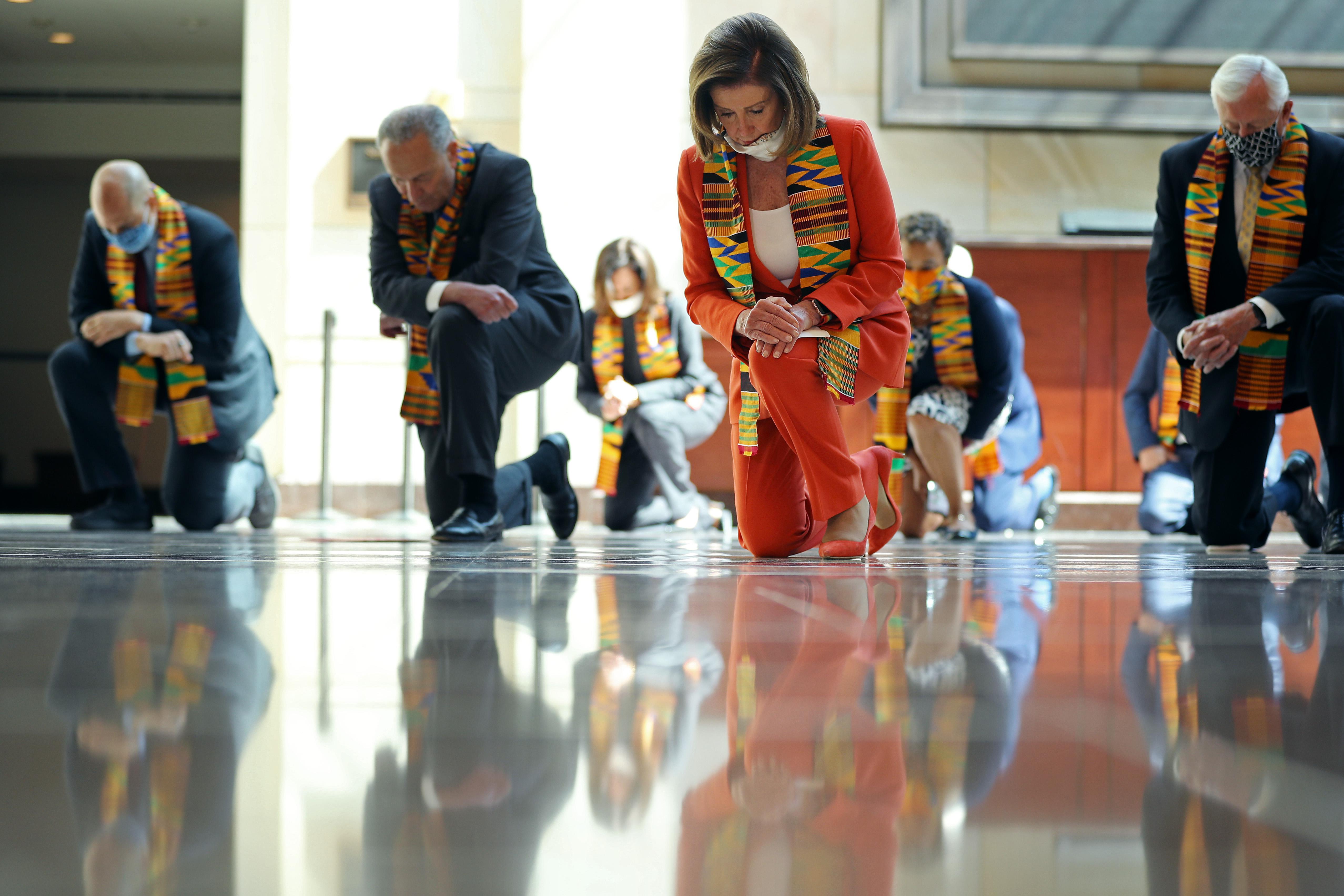 Nancy Pelosi, Chuck Schumer, and other politicians wearing masks and kente cloths take a knee.