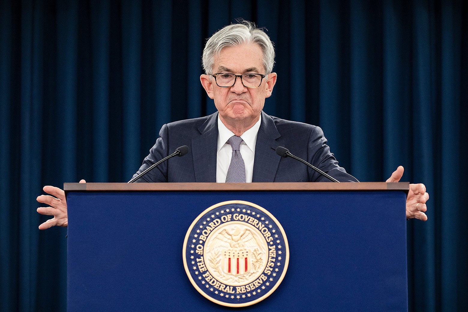 Jerome Powell standing at a podium with a scowl on his face.