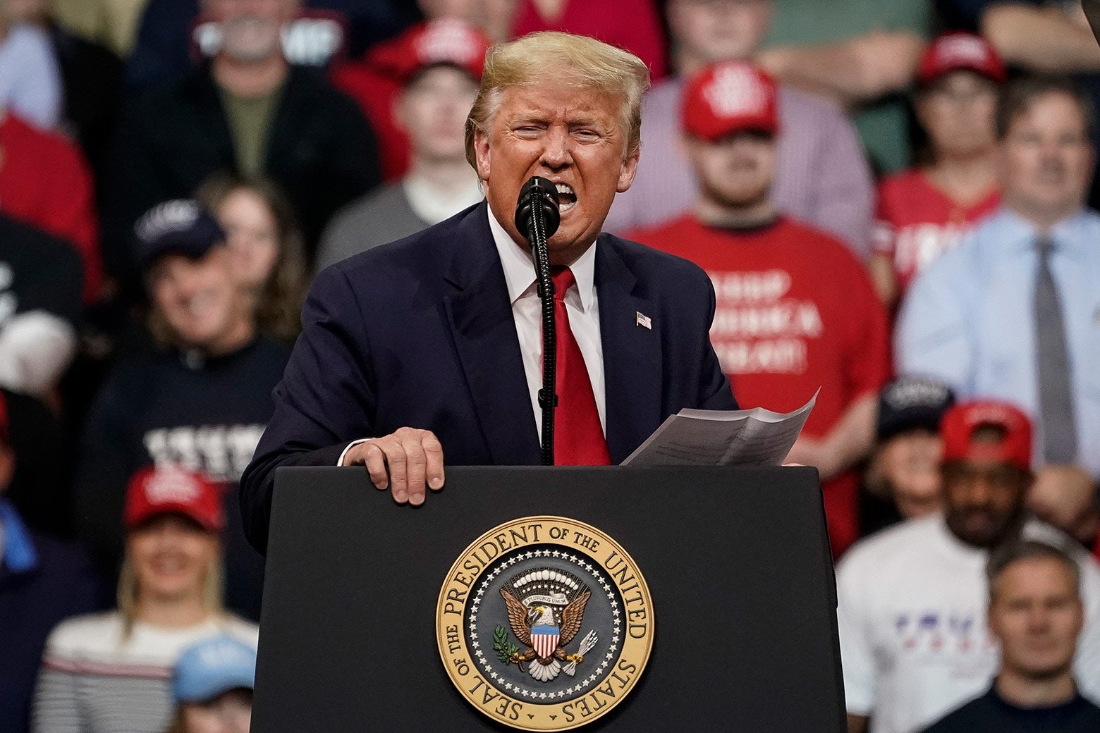 Trump yells into a microphone at a podium in front of a crowd of supporters.