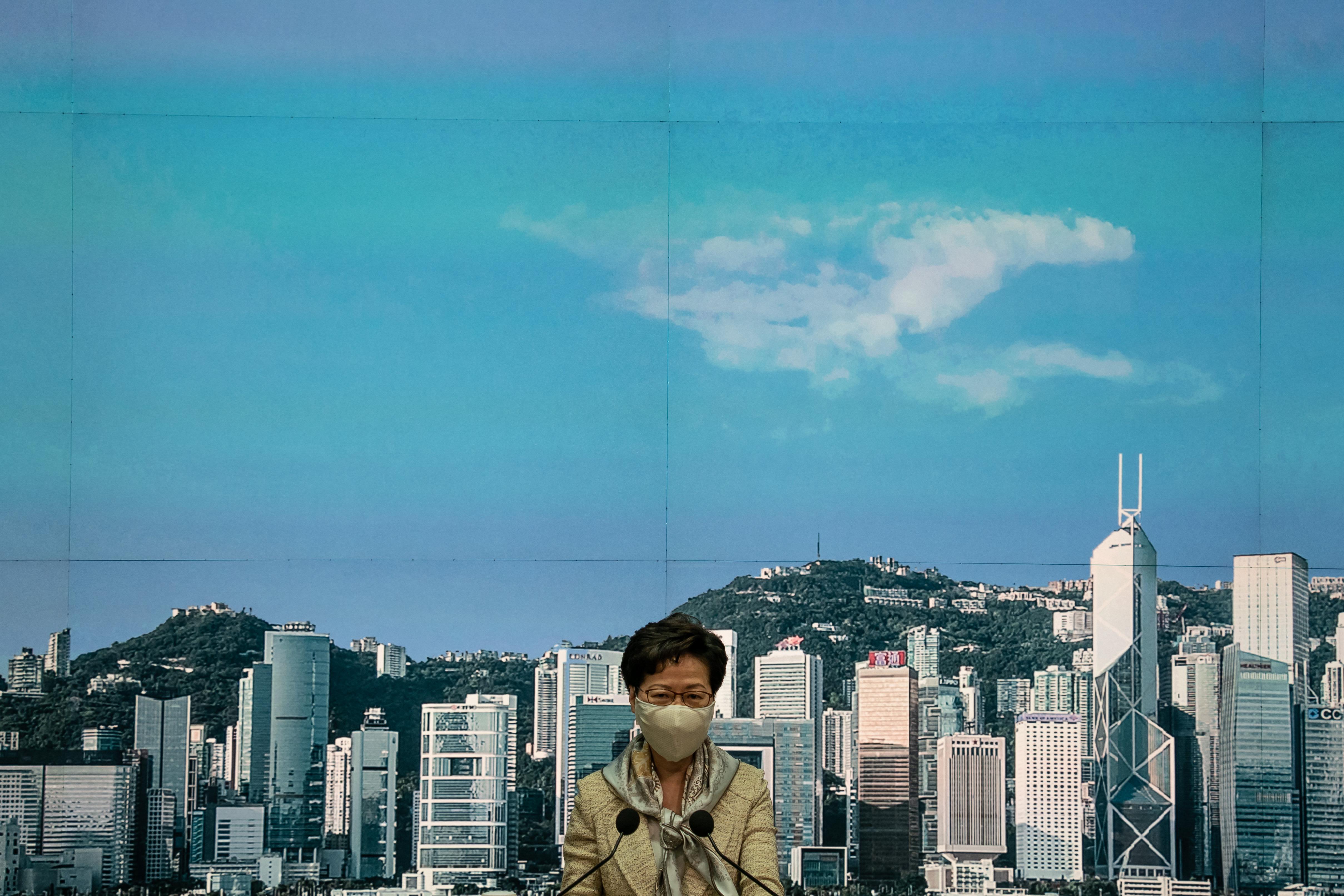 Carrie Lam is seen wearing a face mask. A city skyline is seen in the background.