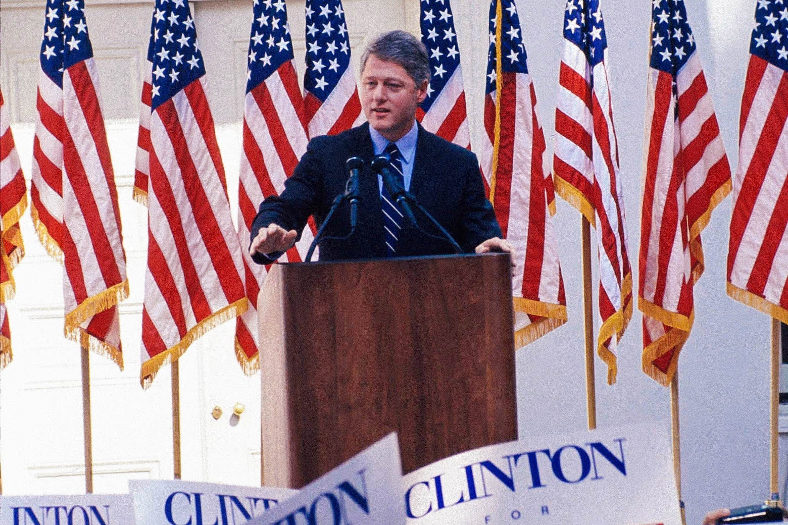 Bill Clinton standing at a podium with American flags behind him.