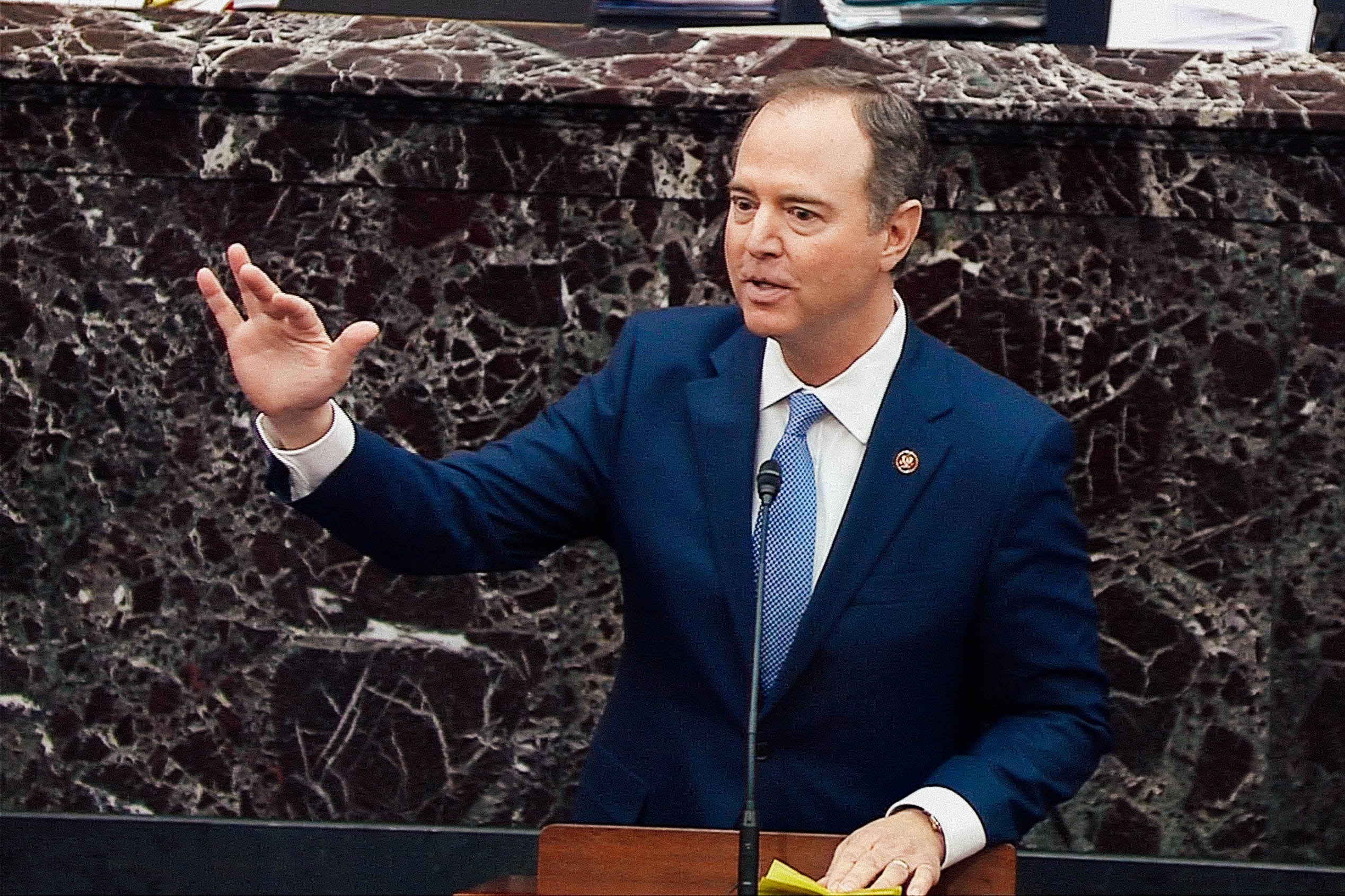 Adam Schiff raises his hand while speaking at a lectern