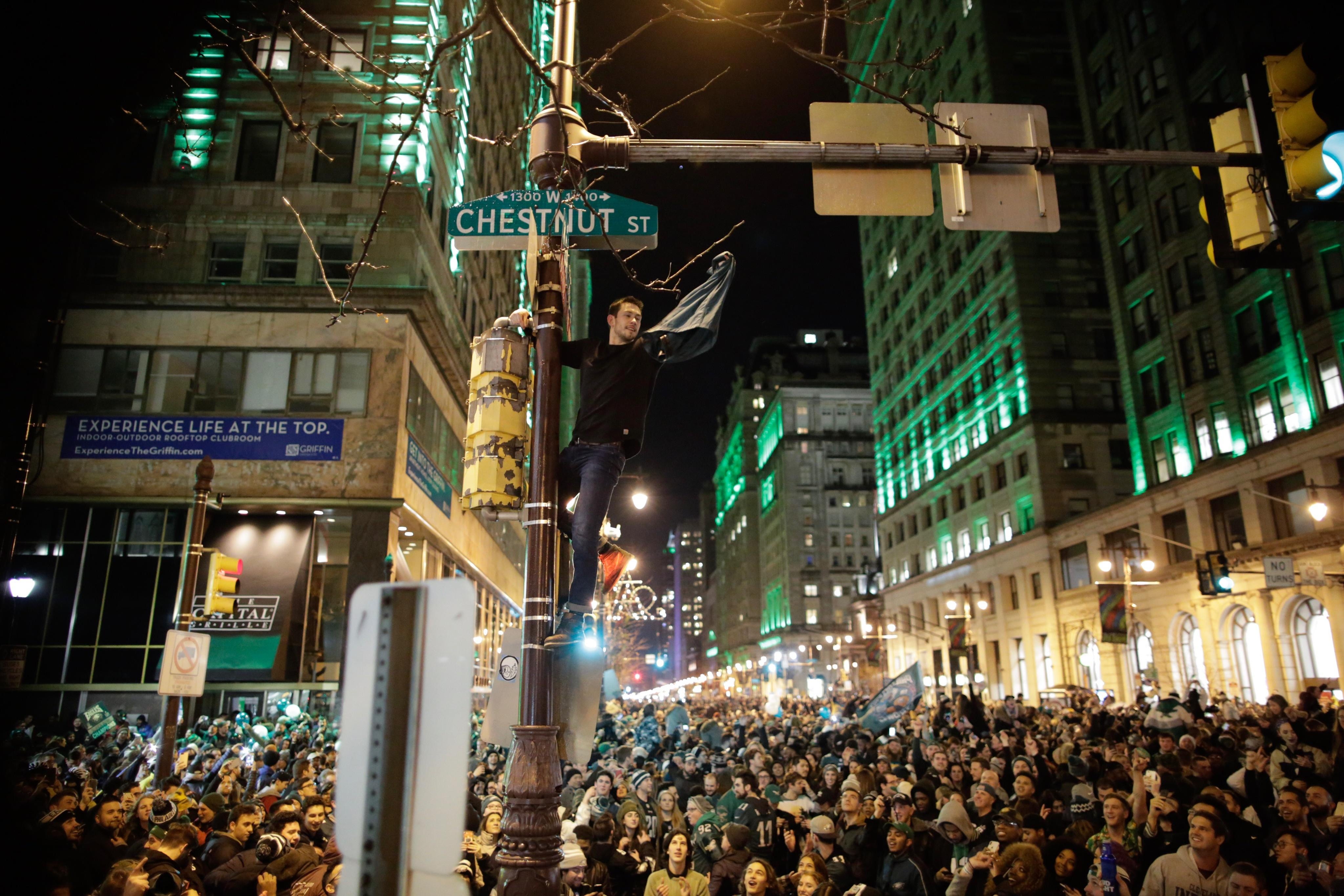 A man atop a traffic pole with his fist raised, a crowd of Eagles fans below him.