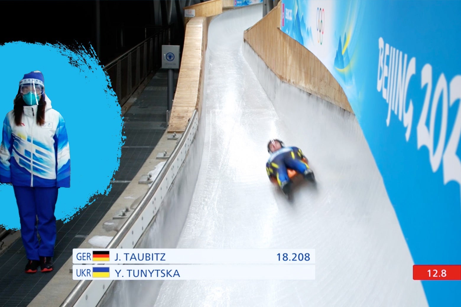 The luge track patroller highlighted beside the track as a luge competitor zooms down the track next to her.