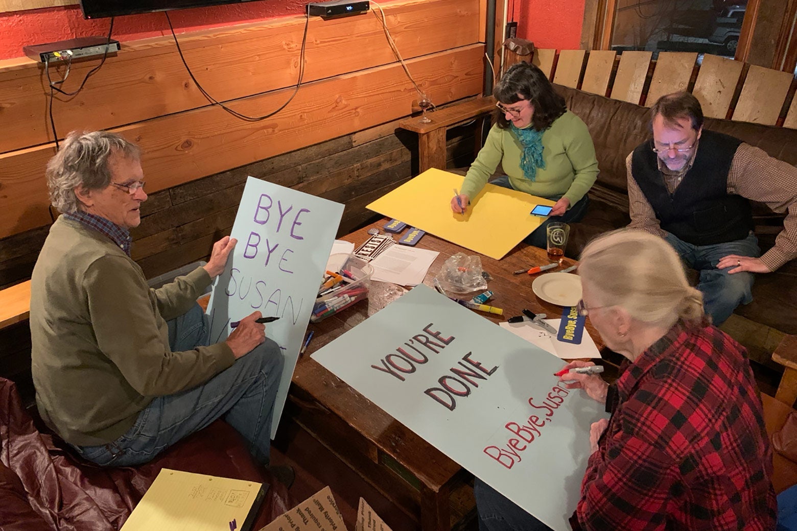 Two men and two women sit around a table making protest signs.