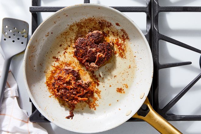 Two burger patties in a greasy frying pan.
