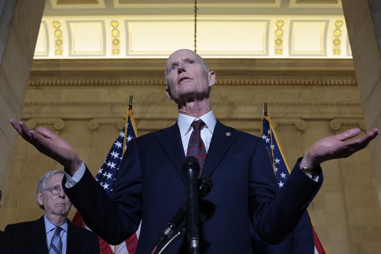 Rick Scott speaks at a lectern as Mitch McConnell looks on behind him