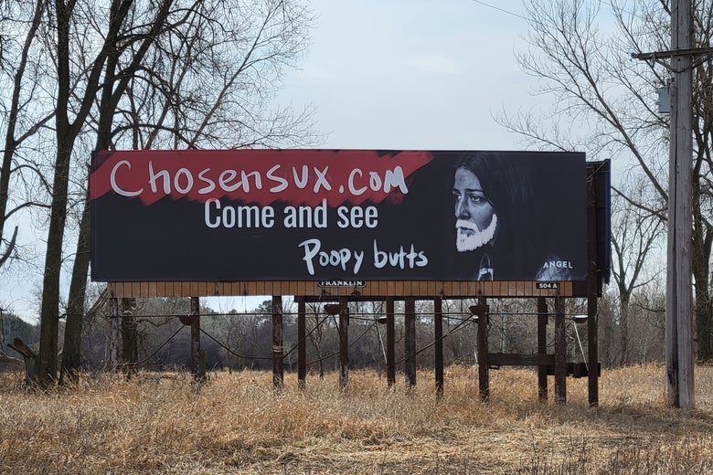 A billboard depicting a figure with a graffiti beard drawn on and the words "Chosexnsux.com Come and see poopy butts"