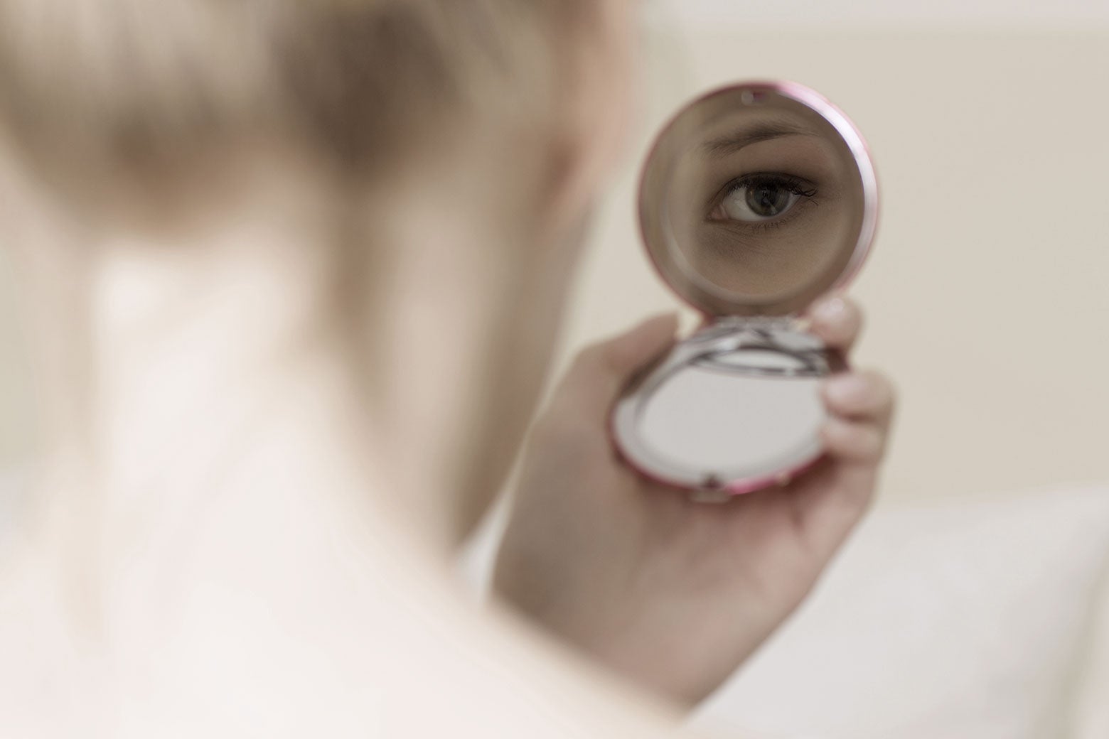 A person looks at their face in a compact mirror.