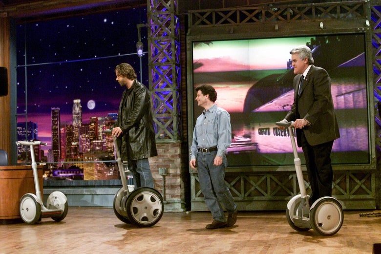 Russell Crowe and Jay Leno ride Segways as Dean Kamen watches.