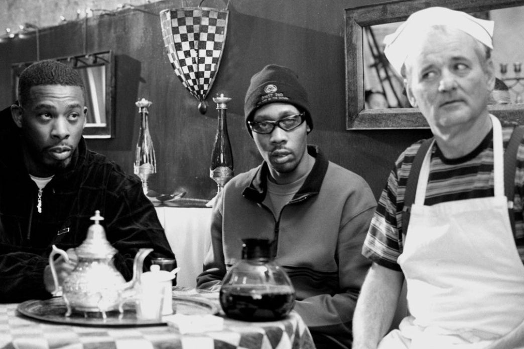 In black and white: seated in a diner at a small table with a checkered tablecloth, from left to right sits hip-hop group Wu-Tang Clan's GZA staring to the right side of the frame, Wu-Tang Clan's RZA, staring straight ahead with a blank face; and actor Bill Murray, dressed as a waiter in an apron and soda jerk hat, looking to the left side of the frame. 