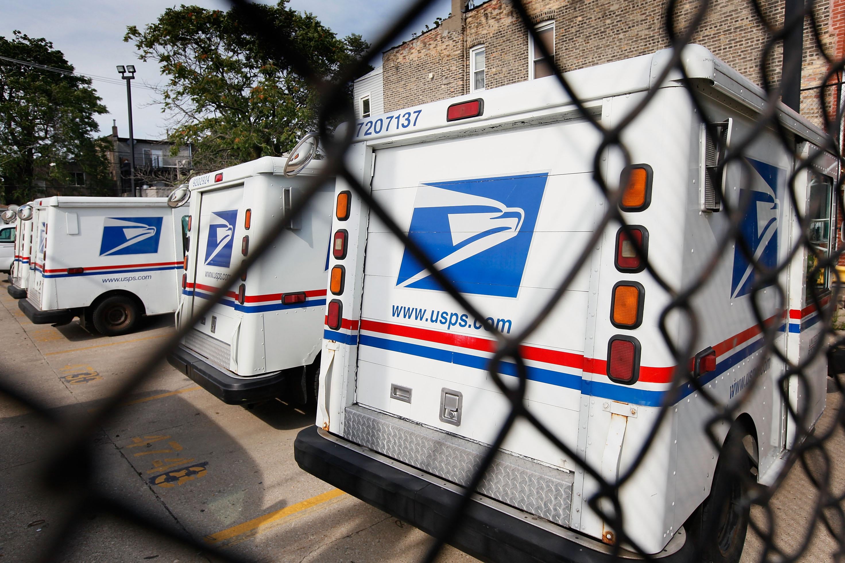 United States Postal Service trucks are seen through a fence.