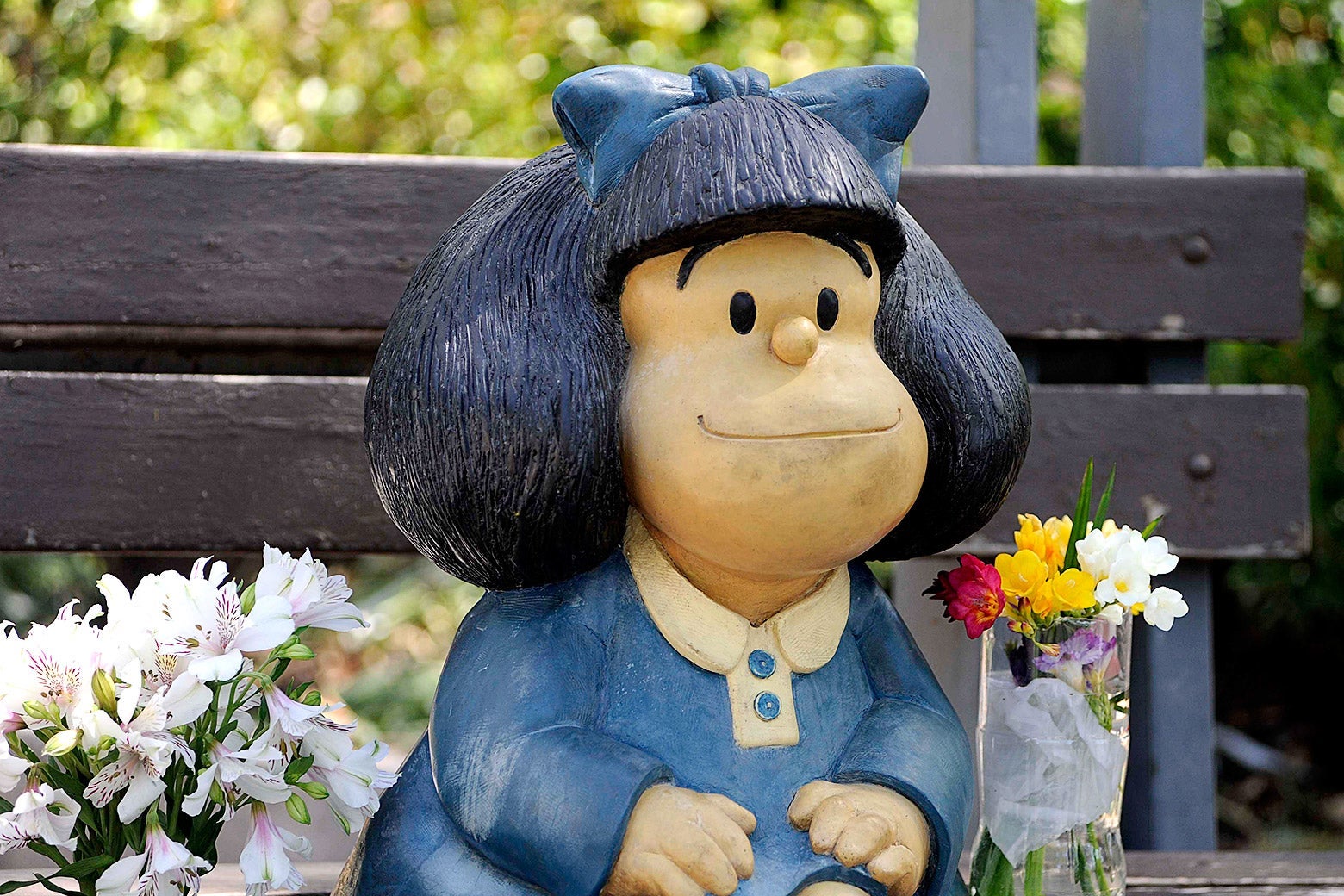 A statue depicting Mafalda is seen on a bench and near some flowers.