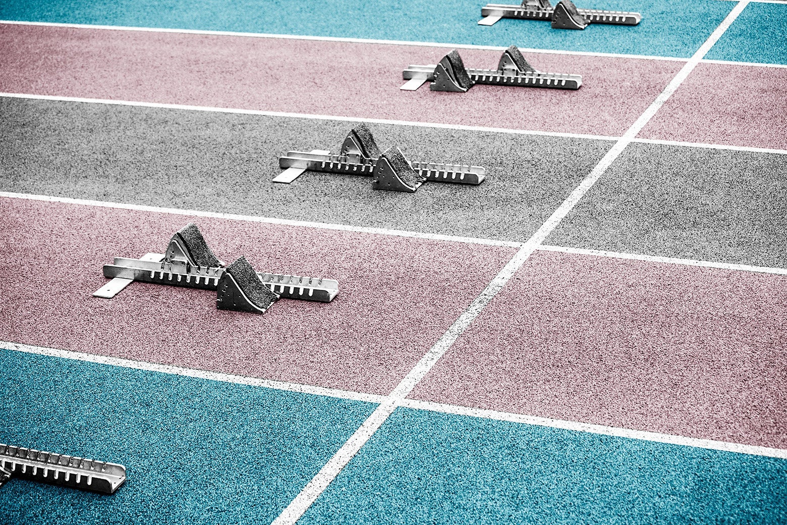 A high school track with lanes painted light blue, pink, and white, the colors of the transgender flag, and starting blocks in each lane