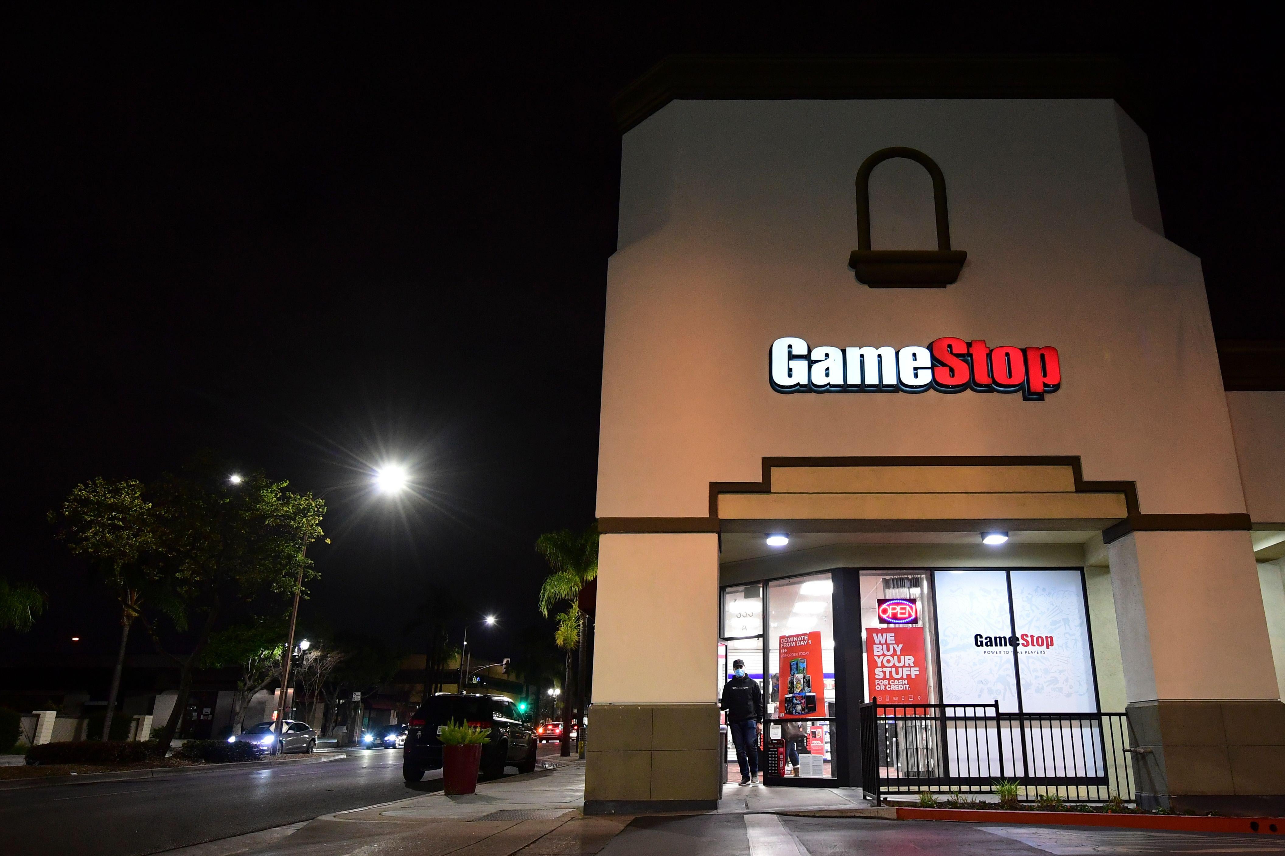 A man stands outside a GameStop store at night.