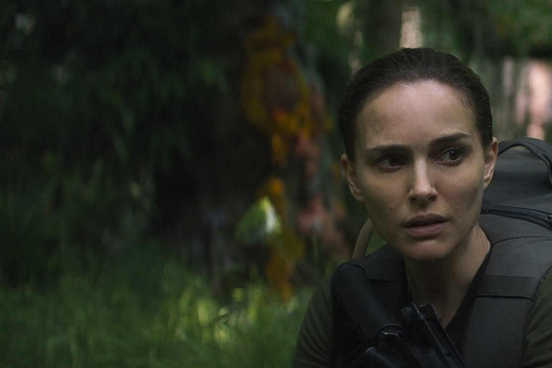 Natalie Portman wears fatigues and holds a gun in a shimmering forest