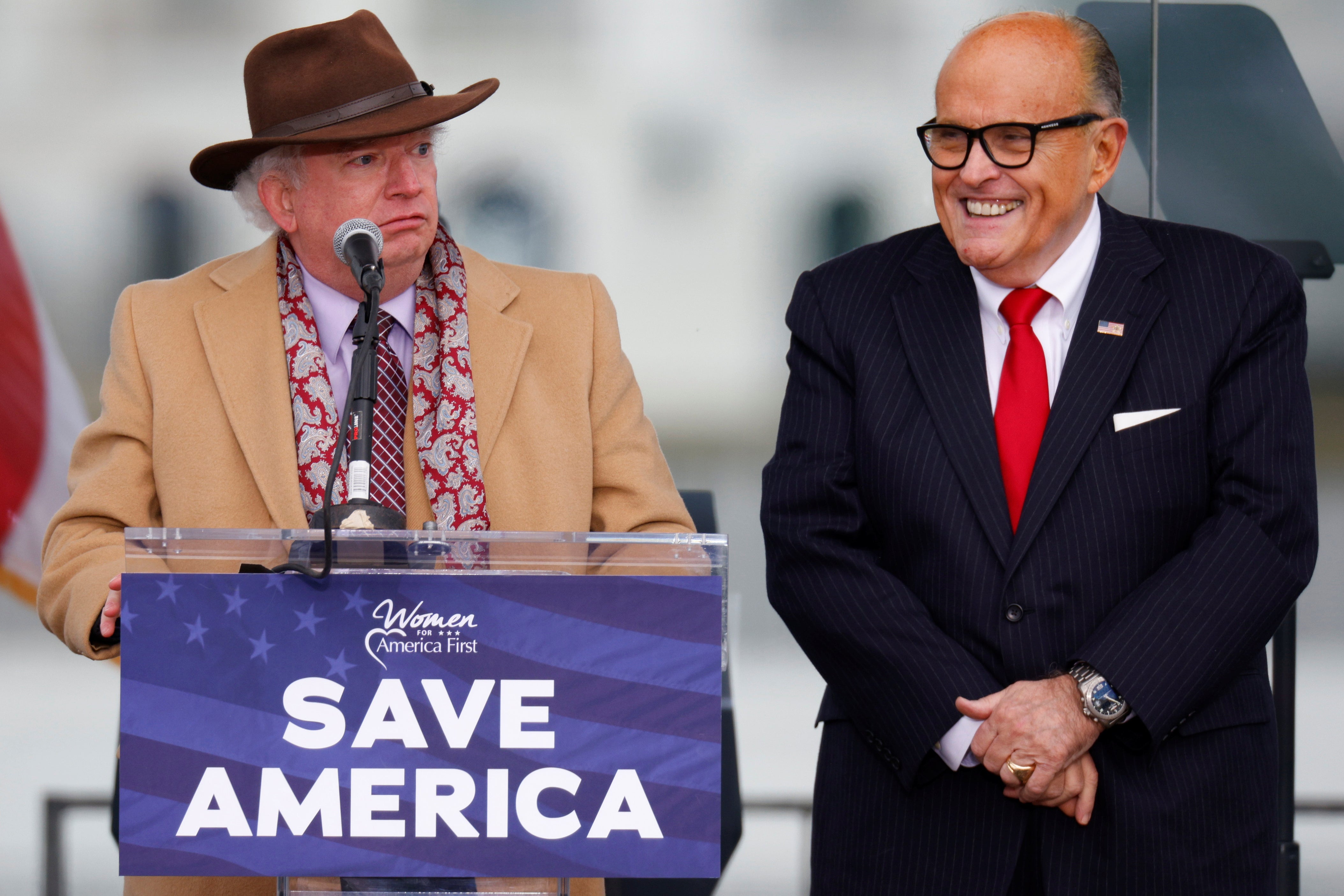 Eastman wears a dumb-looking hat and coat and scowls, Giuliani wears a dumb-looking grin.