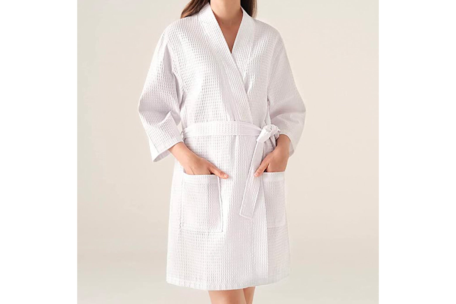 A woman wears a white waffle robe and puts her hands in the front pockets.
