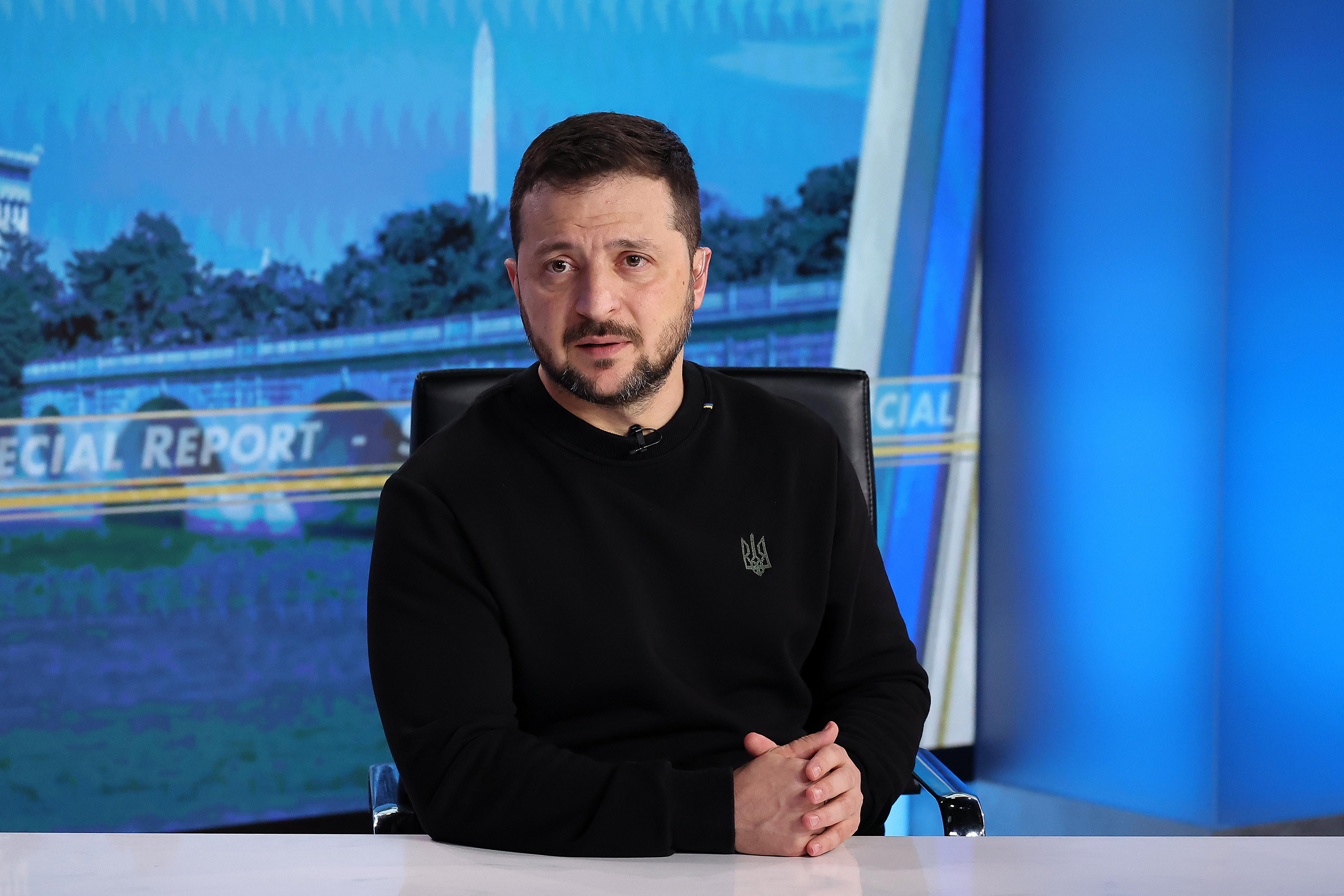 Zelensky on the set of a TV news show in D.C. with the Washington Monument on a screen behind him.
