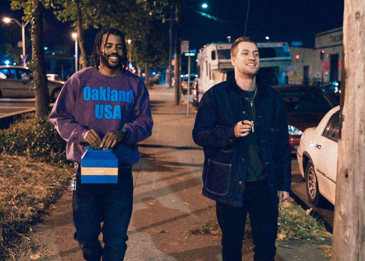 In a scene from Blindspotting, two friends (Daveed Diggs and Rafael Casal) walk down a street in Oakland, California, at night.