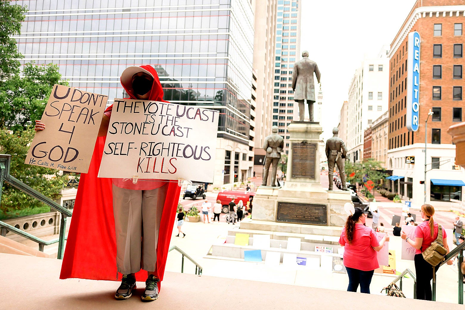 A protestor dressed in a red cape similar to those seen in the TV show The Handmaid's Tale hold up protest signs in favor of religious freedom on the steps of the Indiana statehouse. 
