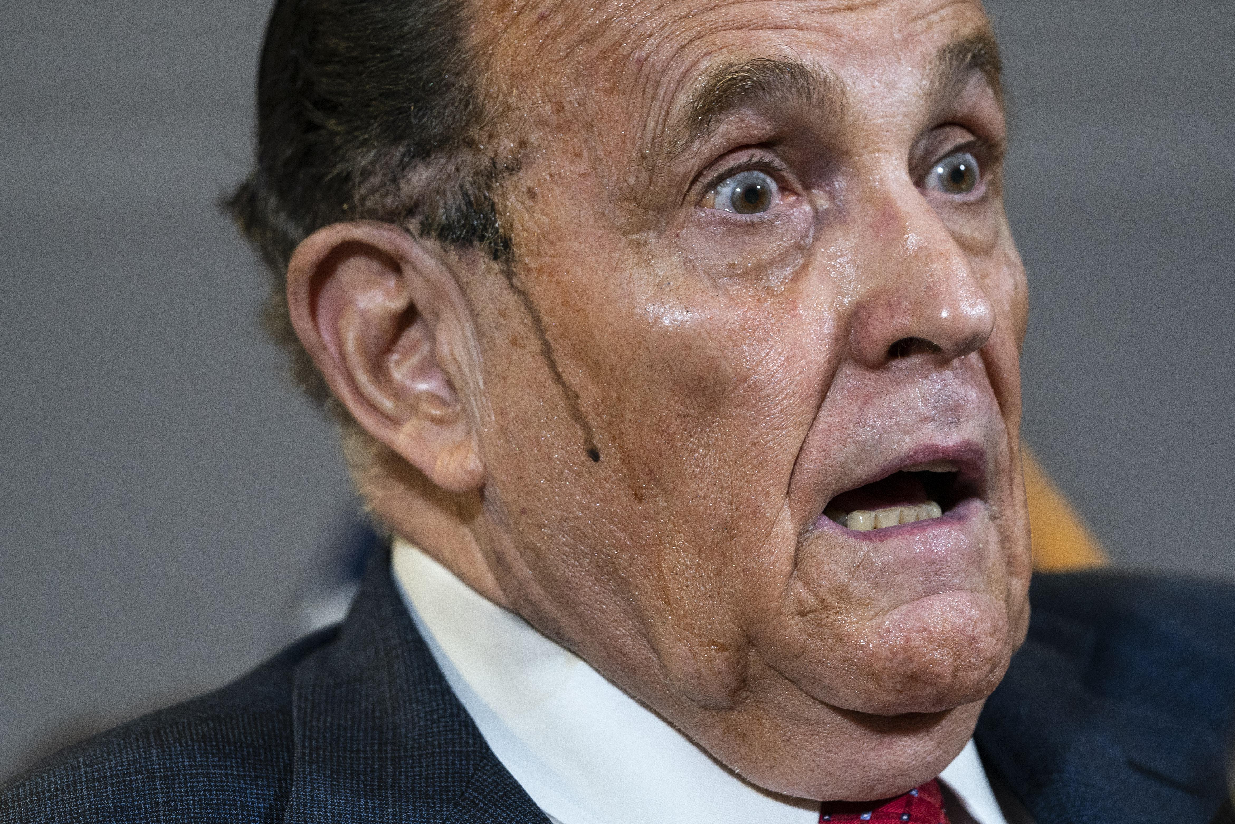 Close-up on Rudy Giuliani looking aghast, with hair dye dripping down the side of his face, during a press conference