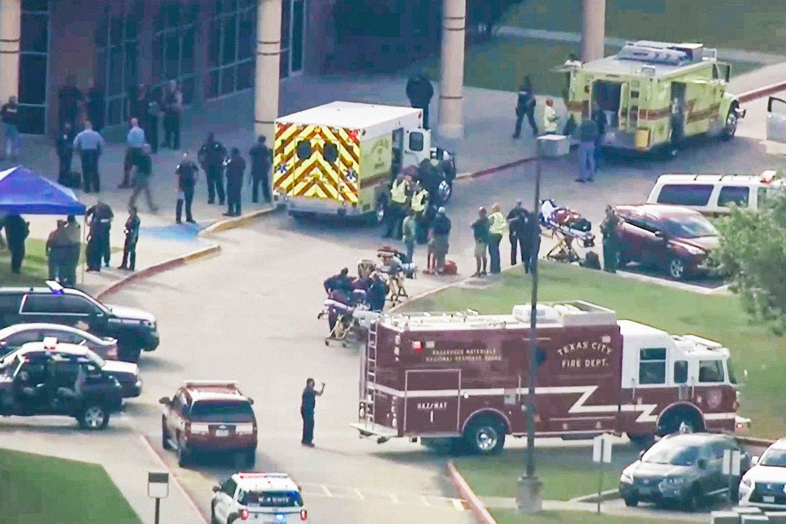 A fire truck, ambulances, and police cars outside a high school as seen from a helicopter.