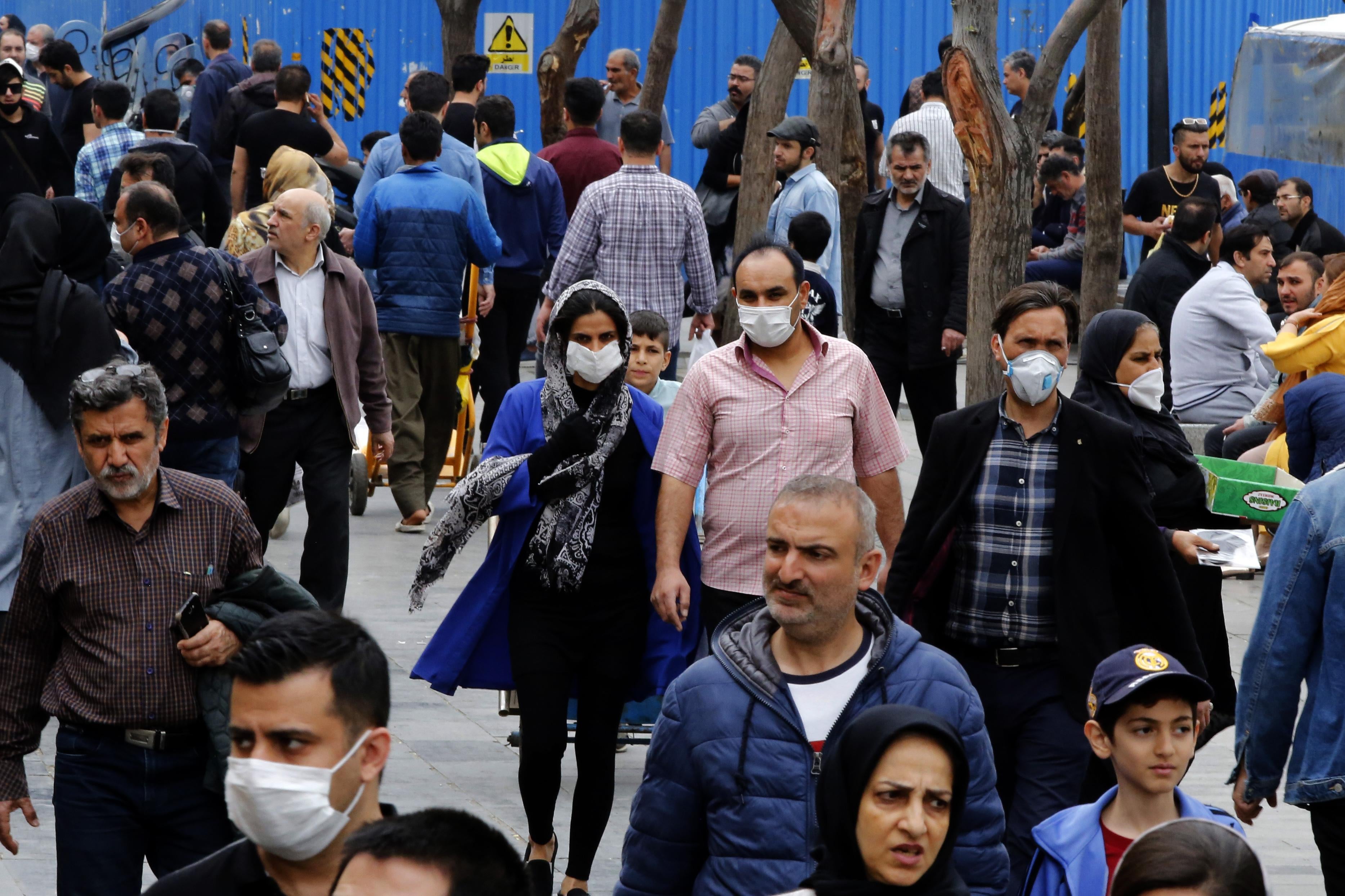 Iranians, some wearing protective masks, walk down the street in Tehran.