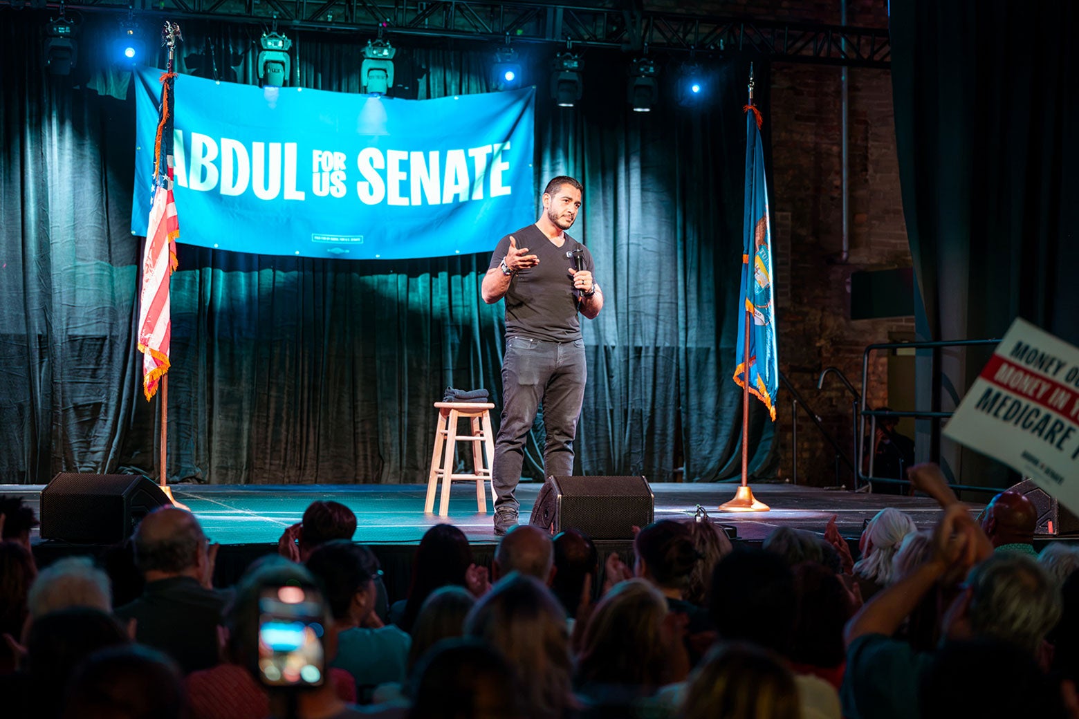 Abdul El-Sayed stands onstage in jeans and a black T-shirt at a campaign event.