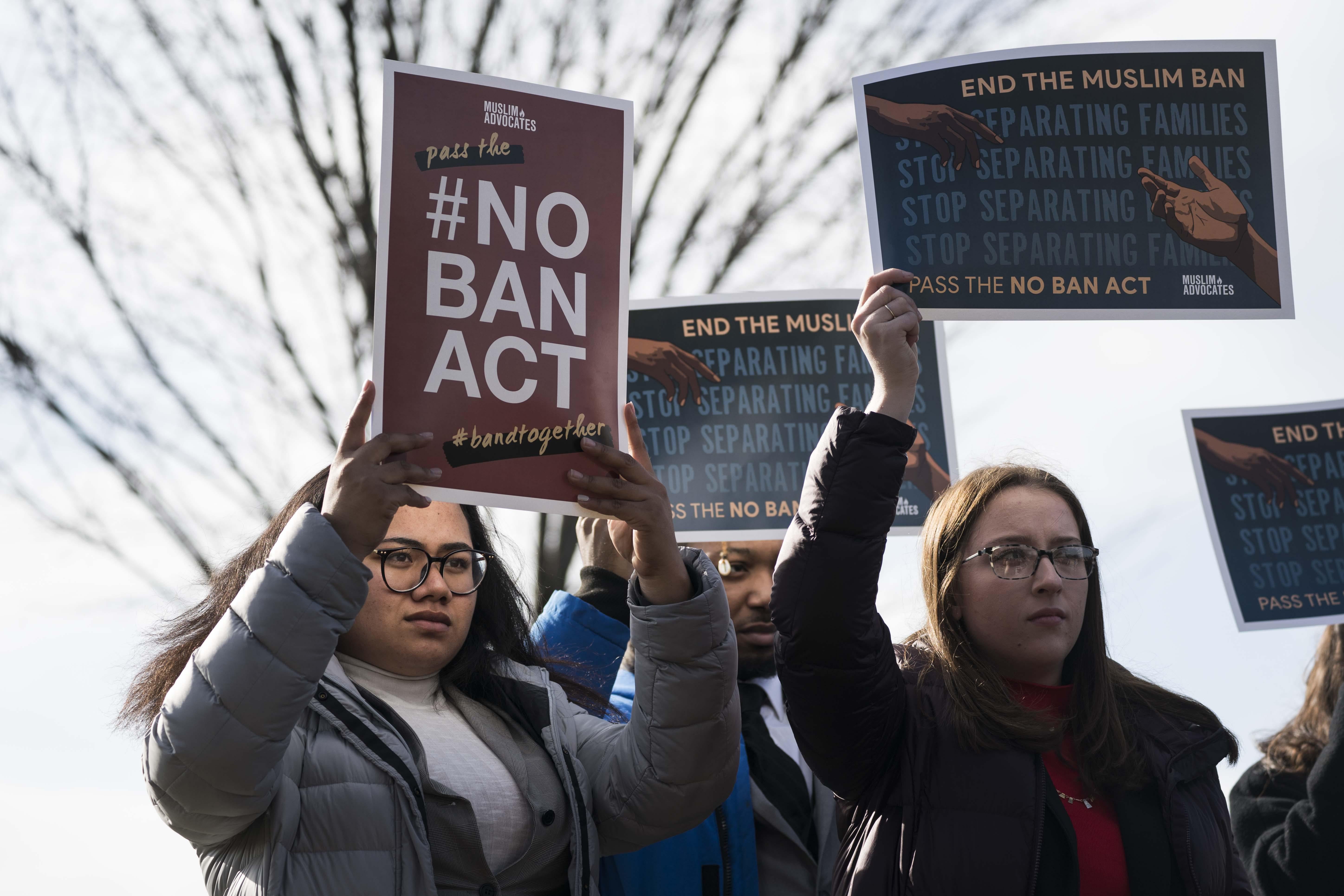 People hold signs reading "#NoBanAct" and "End the Muslim Ban."