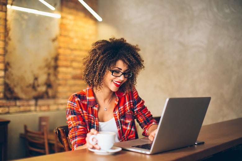 a woman smiling at her computer screen and drinking coffee