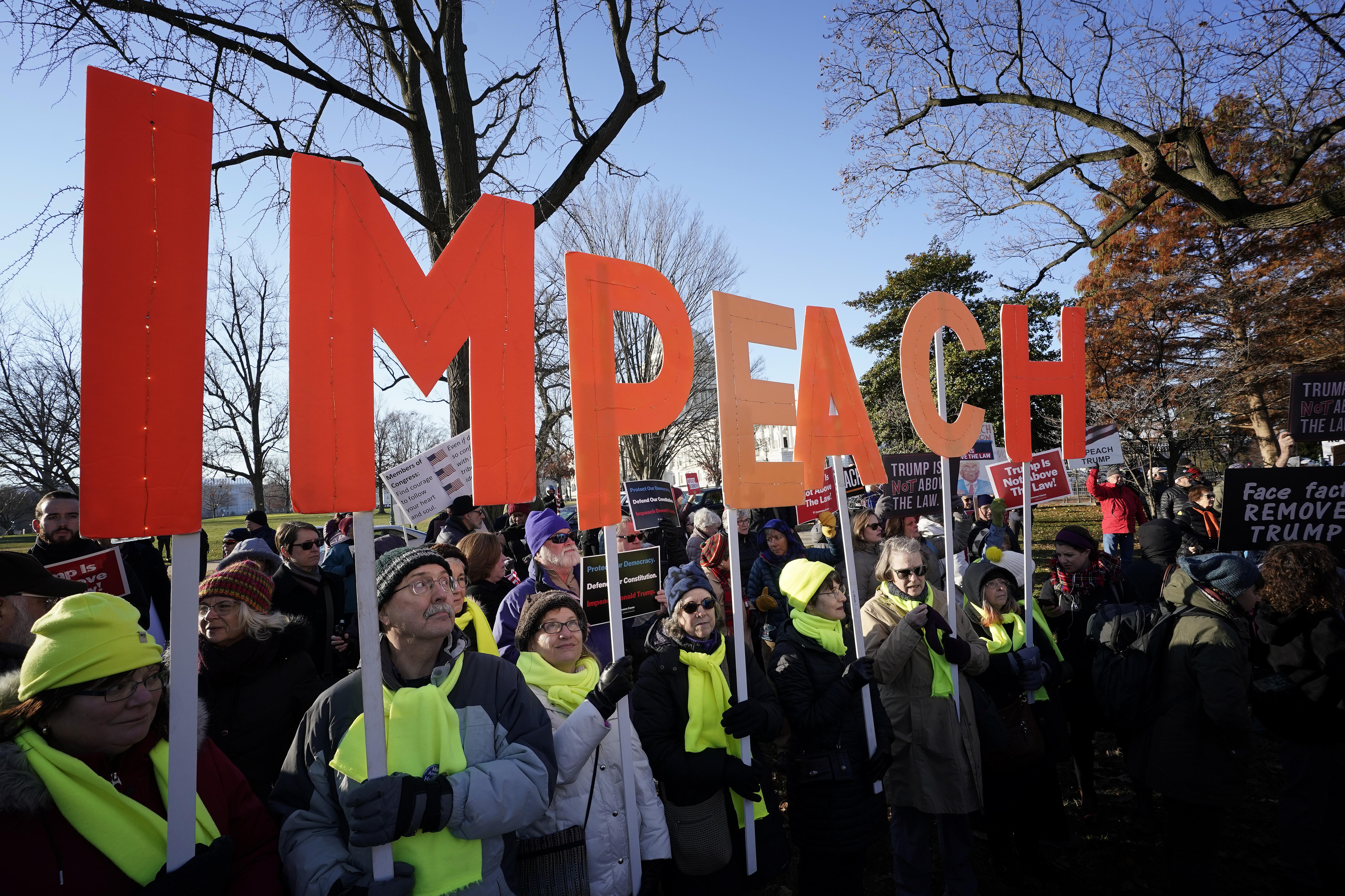Protesters outside the capitol hold signs that read "IMPEACH."