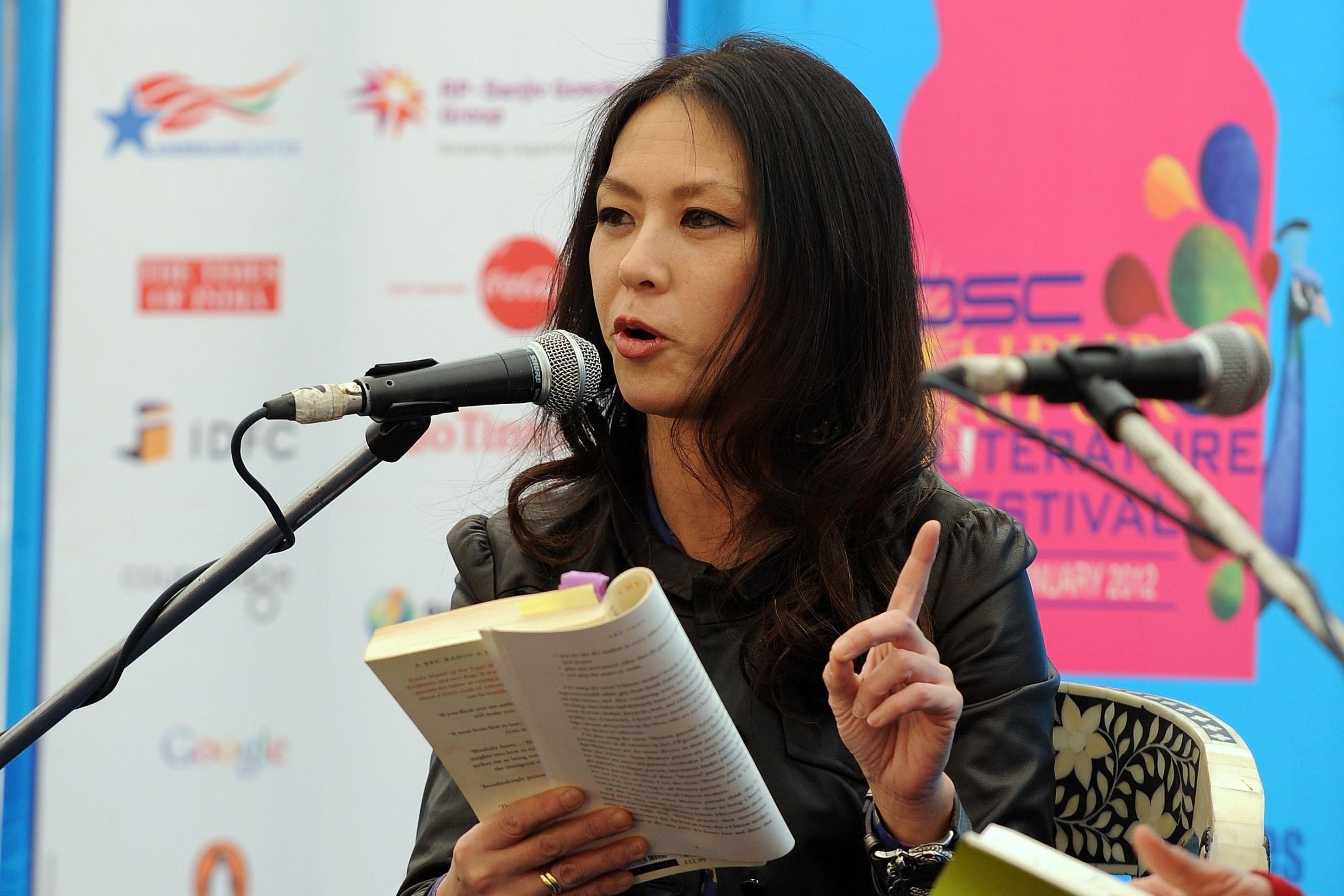 Amy Chua gestures with one hand as she reads from her book at a mic.