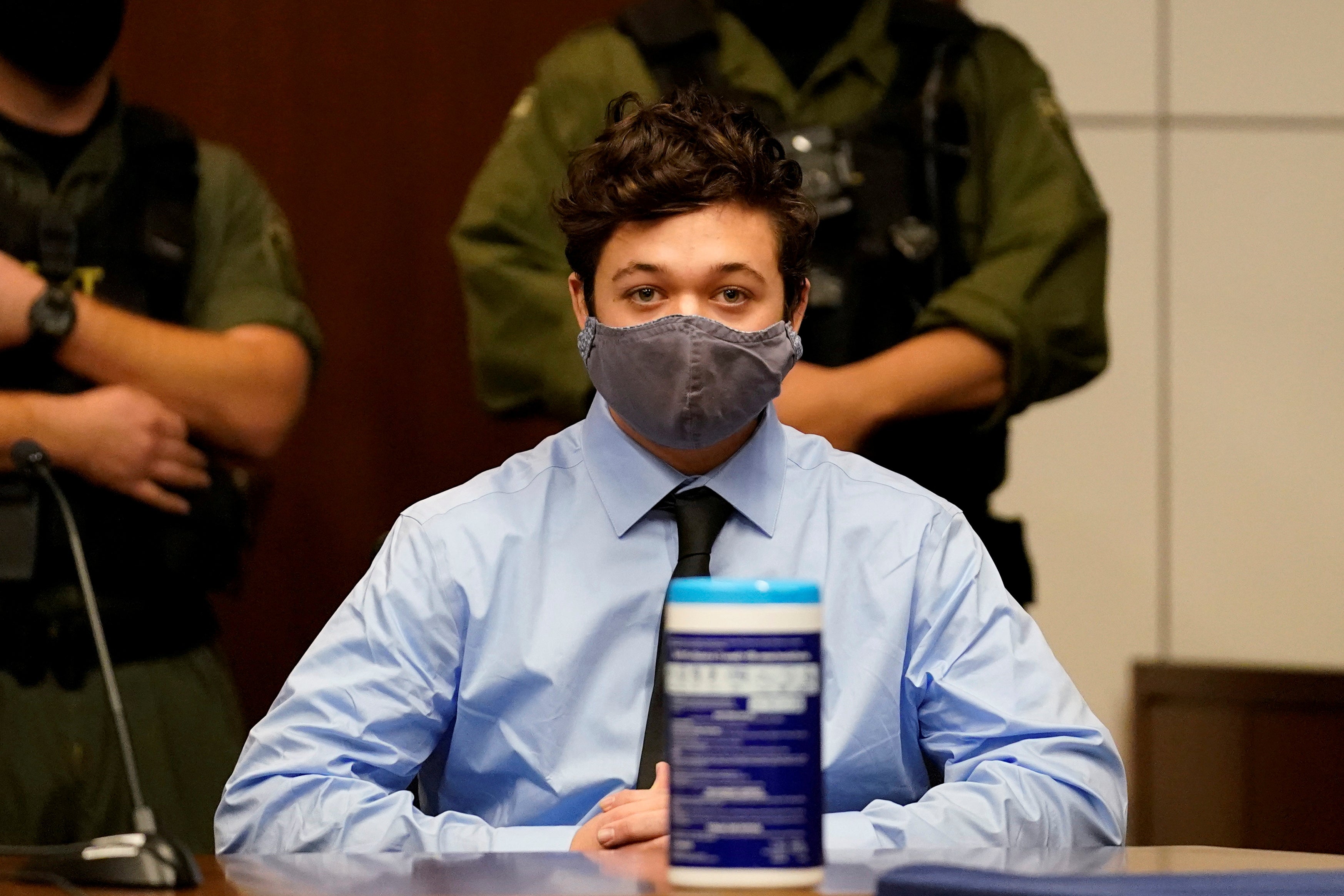 Kyle Rittenhouse, wearing a dress shirt, tie, and mask, sits during a court hearing.