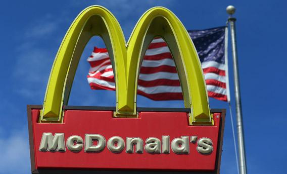 A sign for a McDonald's restaurant sits in front of an American Flag.