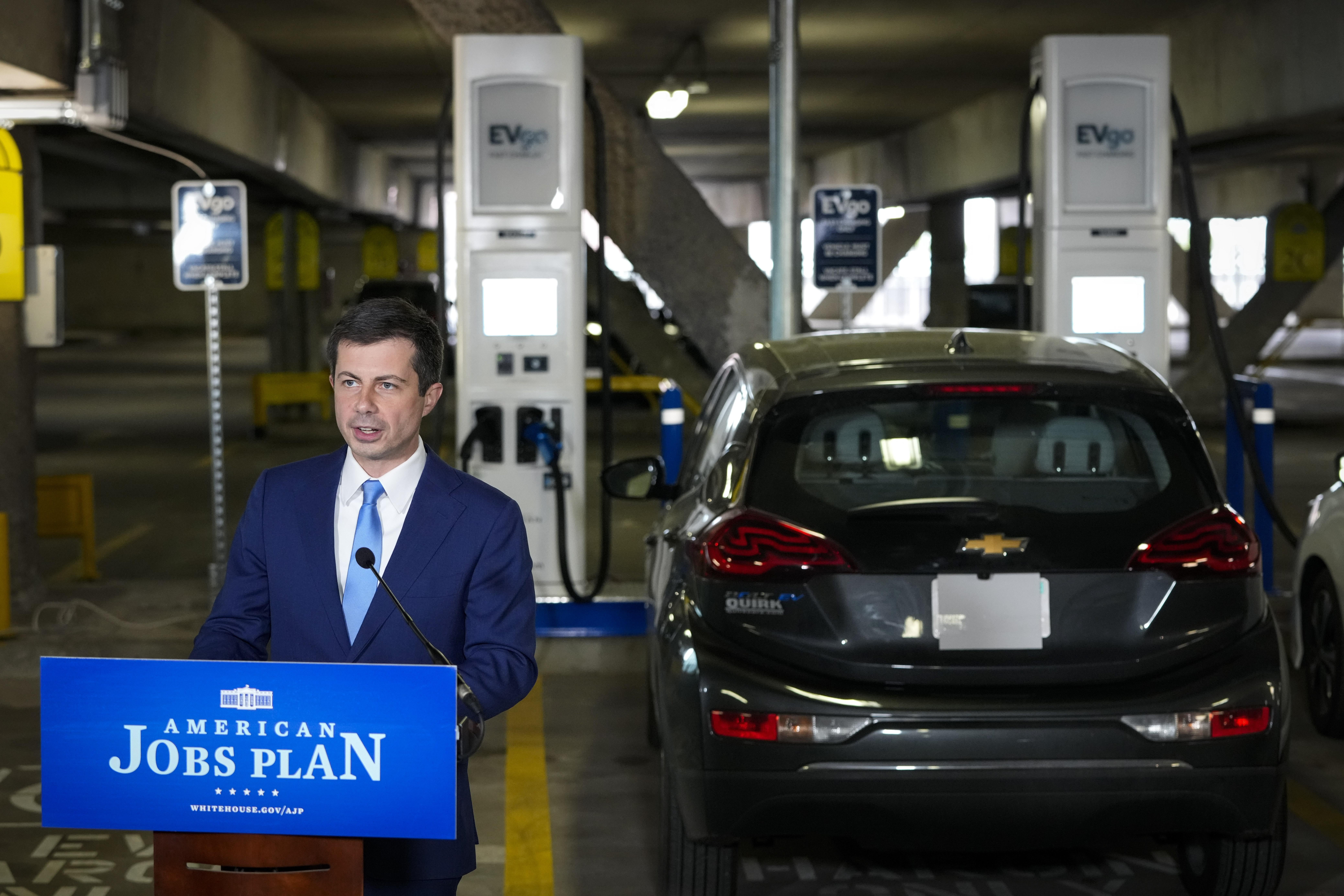 Pete Buttigieg speaks at a podium next to an electric vehicle charging station at Union Station in D.C.