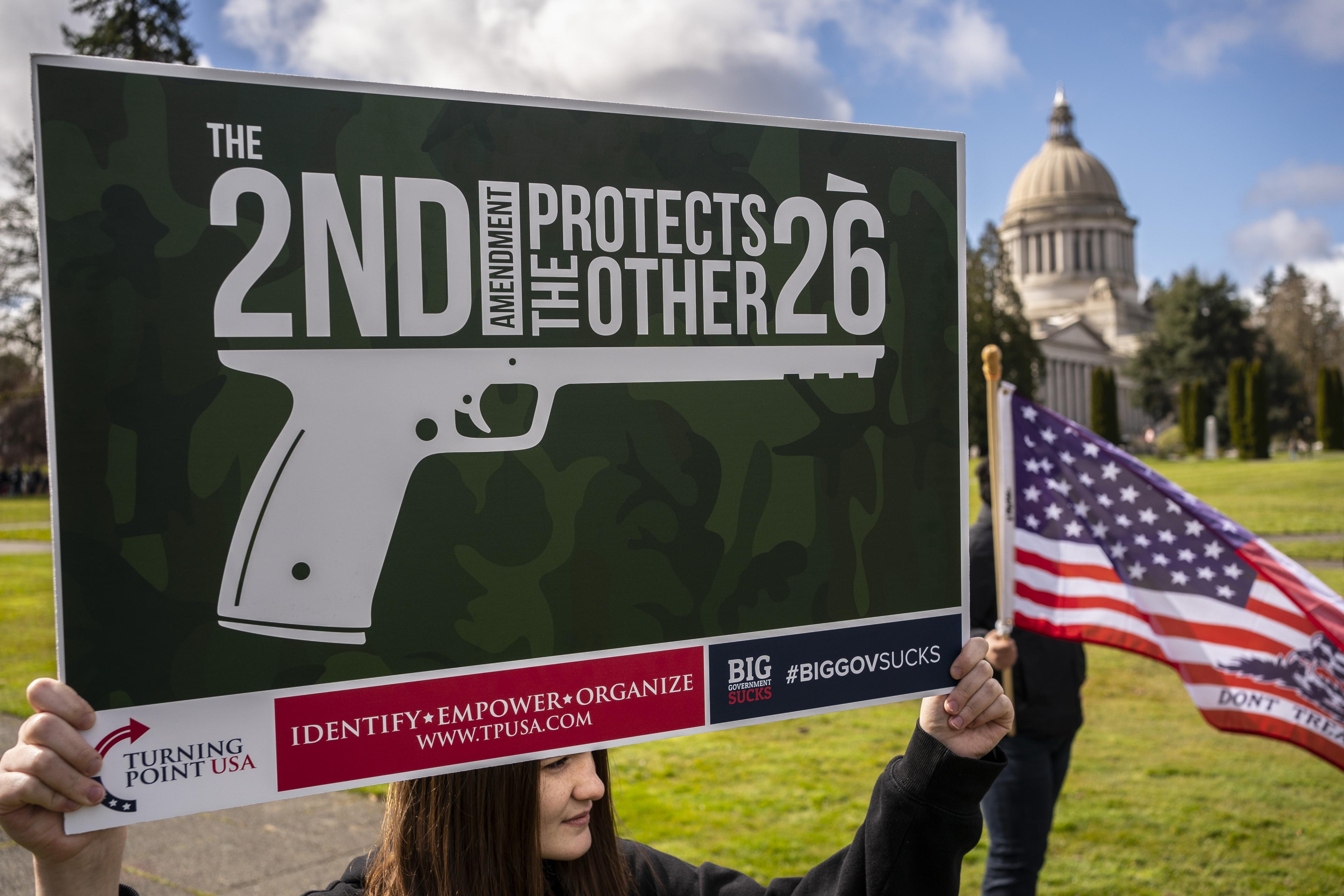 Woman holds up sign that reads "The 2nd Amendment Protects the Other 26" with the words shaped like they're part of a gun.