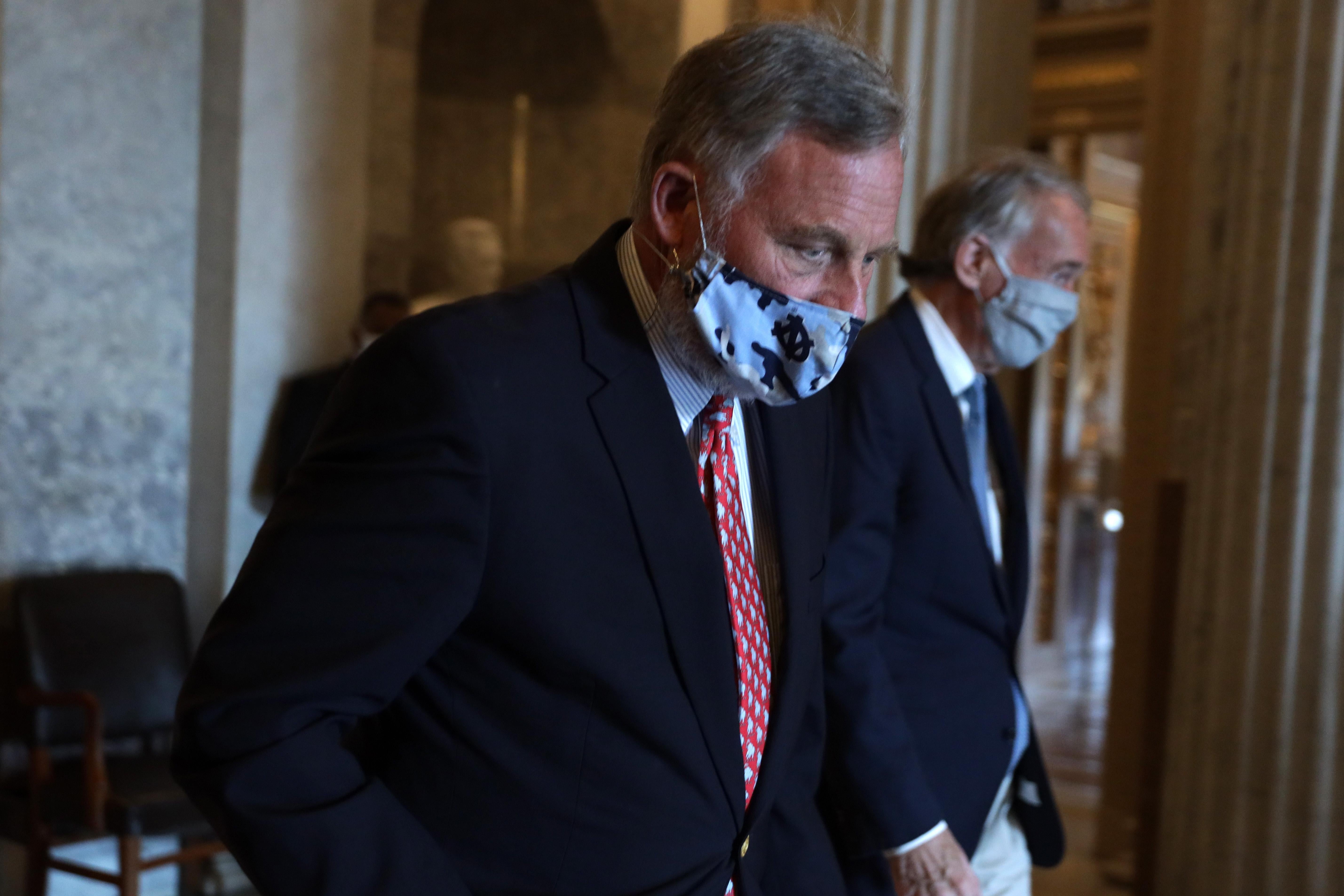 Burr walking with his eyes down, face covered by a mask.