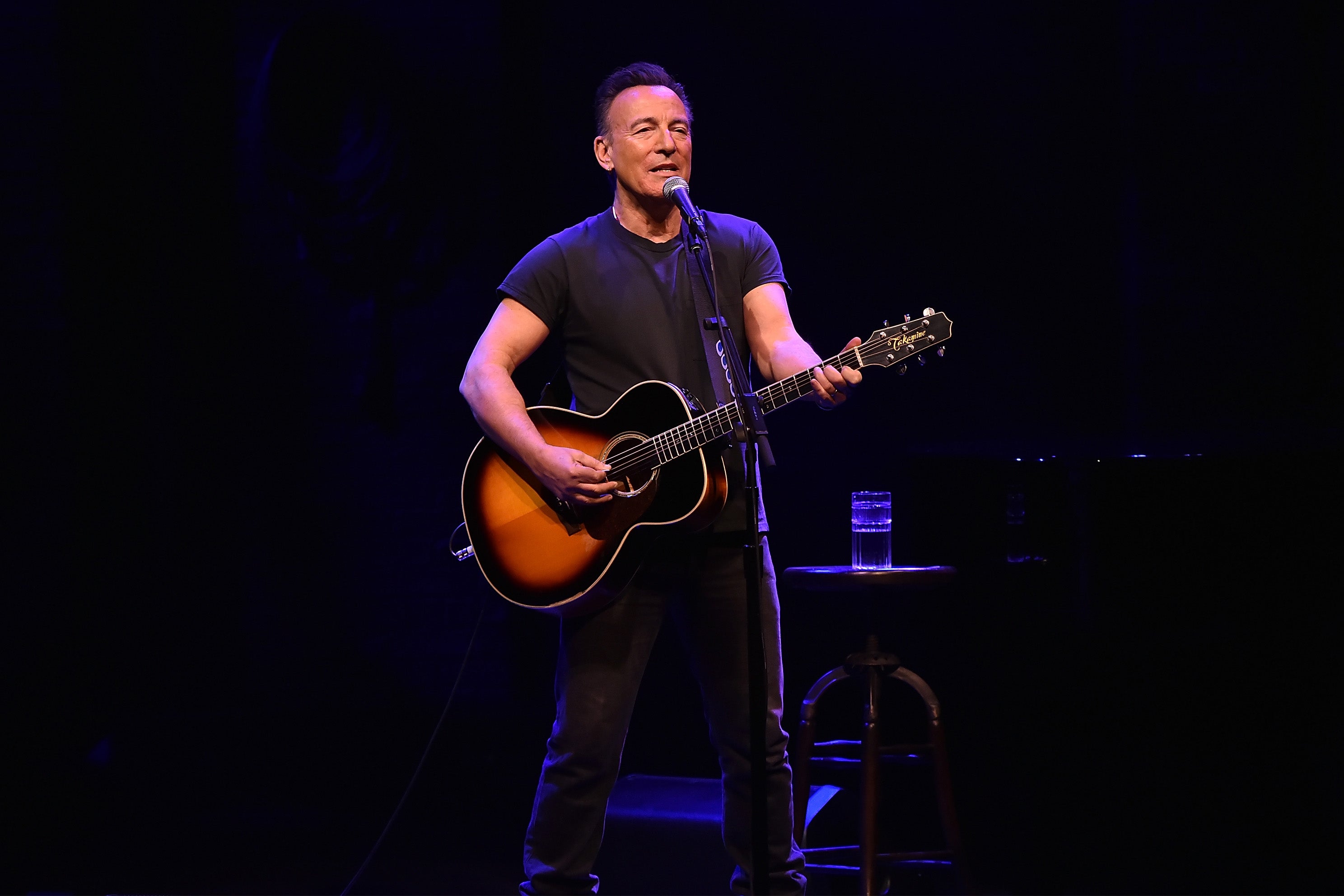 Bruce Springsteen, wearing all black, plays guitar and sings.