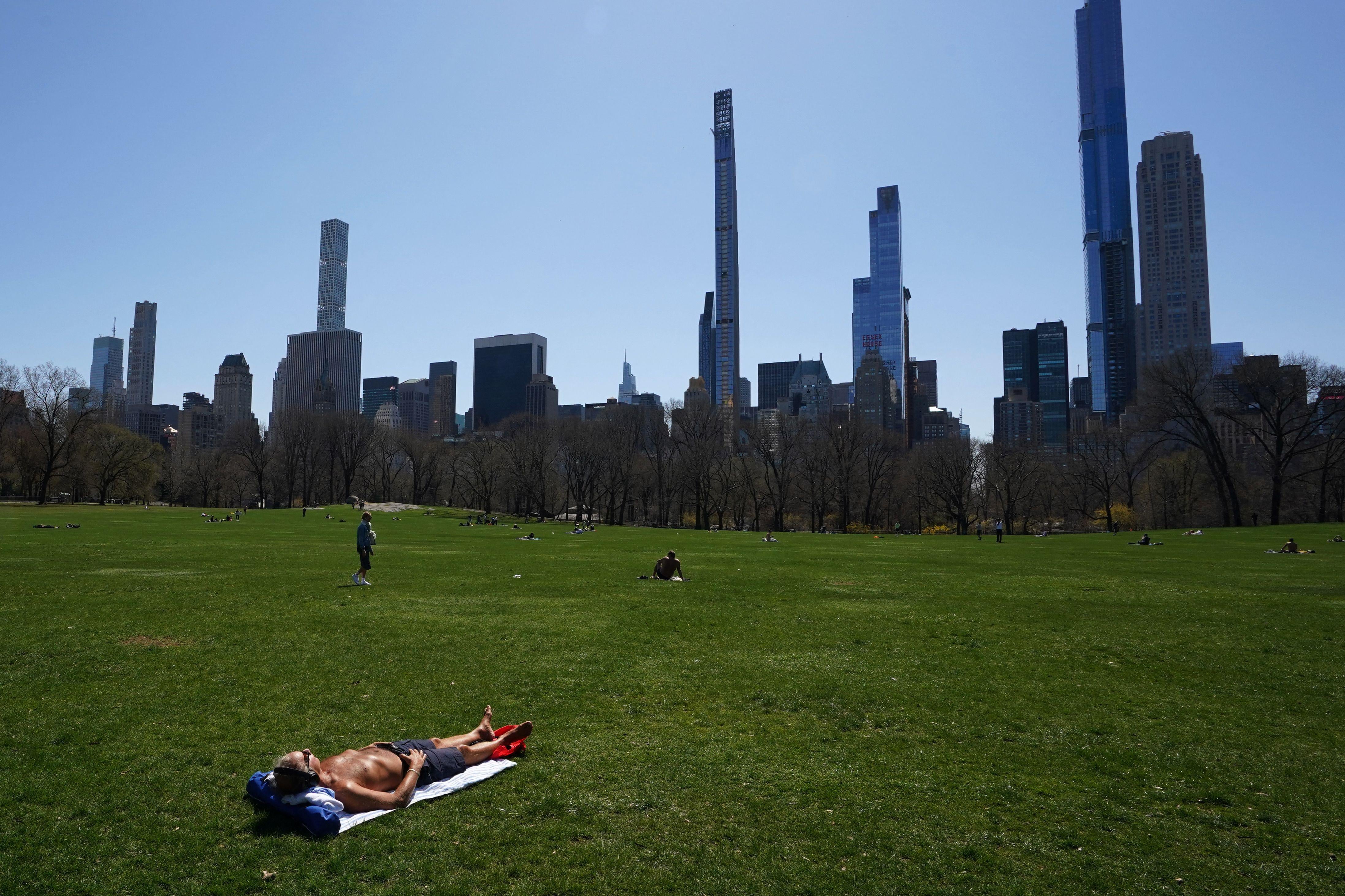 A shirtless man lays alone, far away from anyone else, on the grass in the meadow of Central Park.