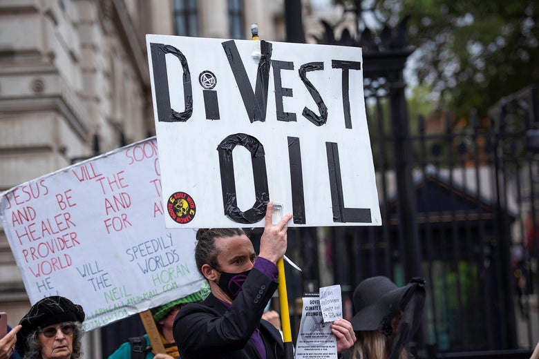 A man with a face mask holds a sign that reads "Divest Oil."