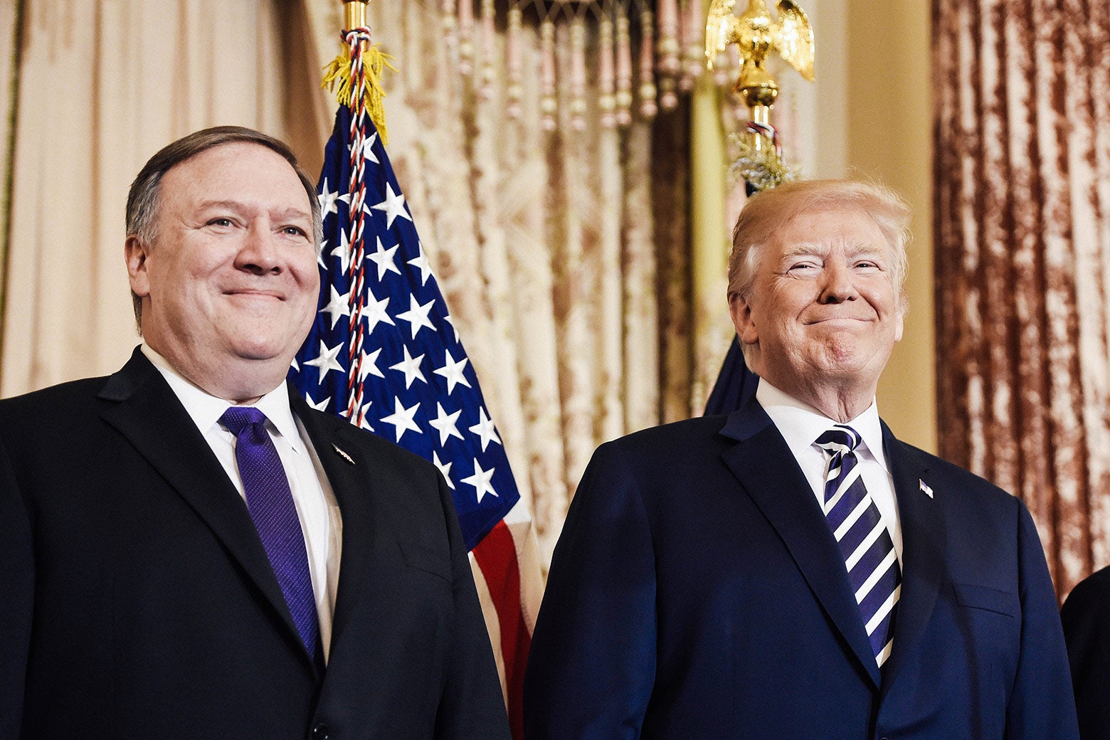 Mike Pompeo stands beside Donald Trump in an ornate room.