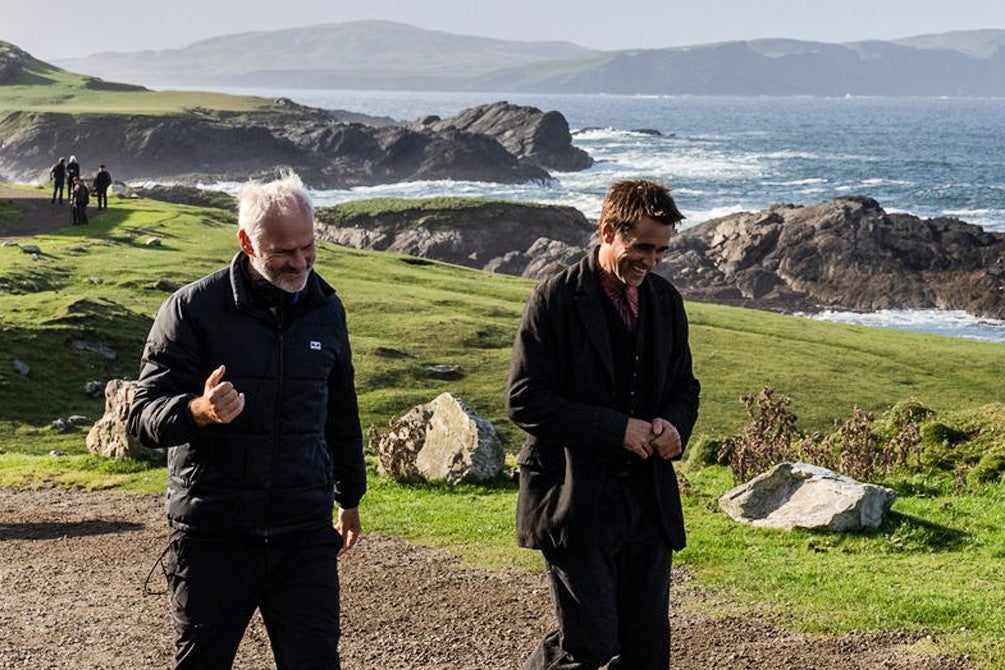 Two men walk along a rocky green Irish coastline.