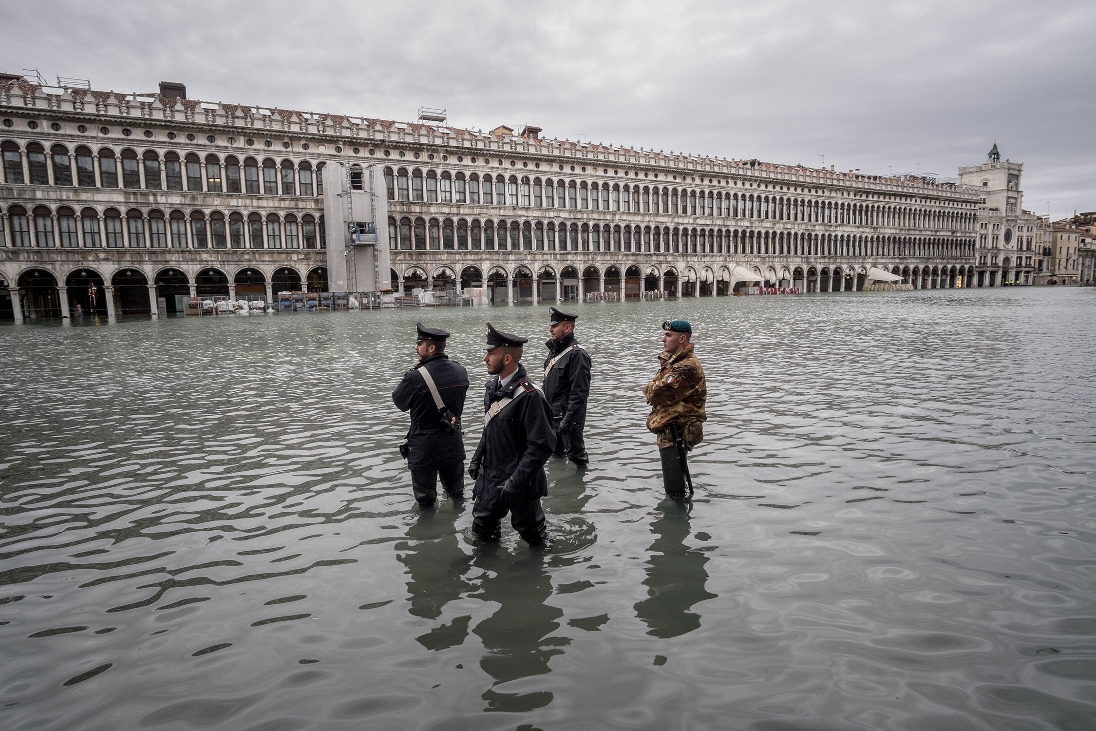 Four law enforcement agents patrol a flooded St. Mark's Square, Nov 17th 2019, Venice. The water reaches their knees.
