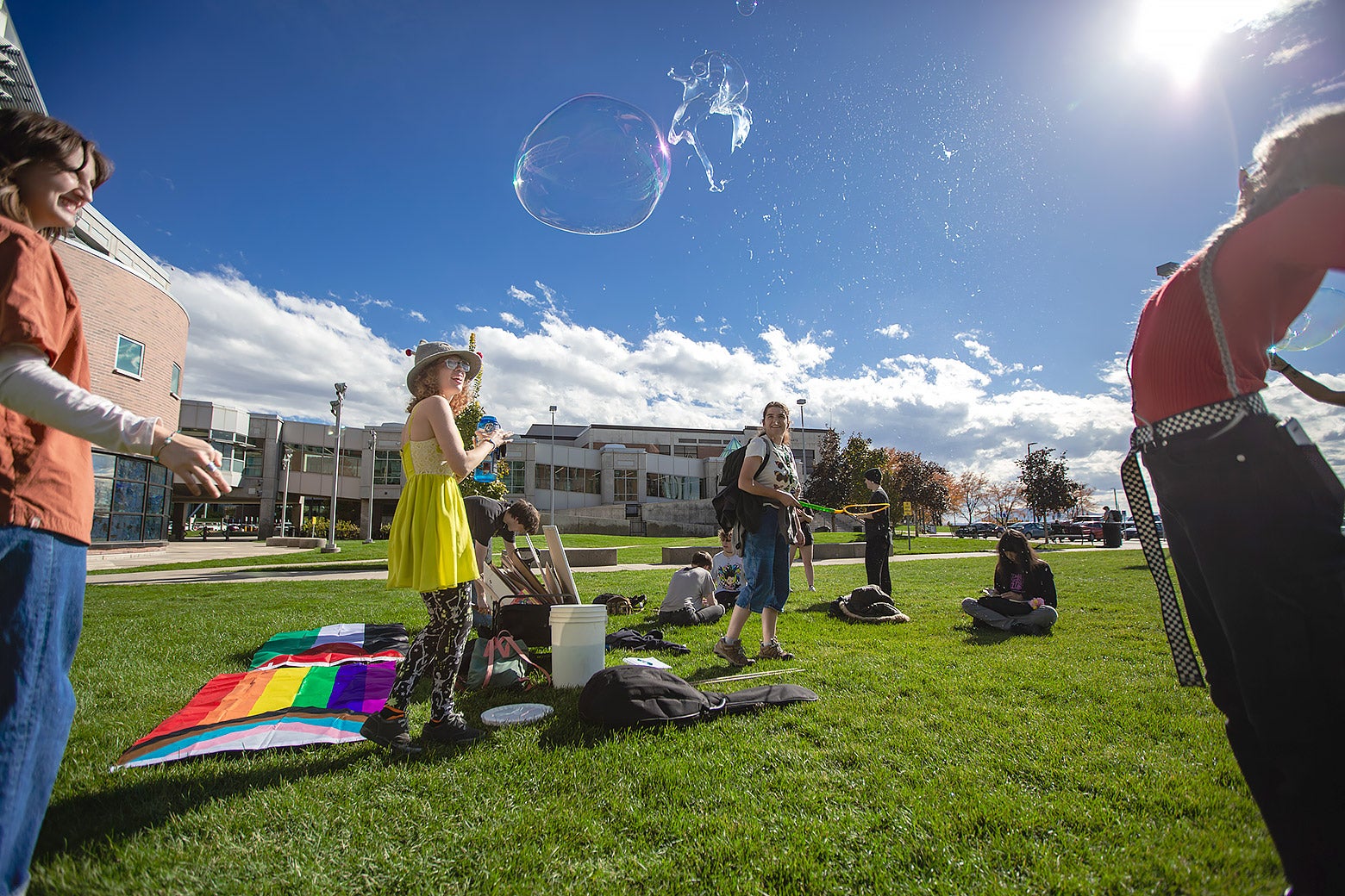 A small gathering of students on the grass around a Pride flag and bubbles.