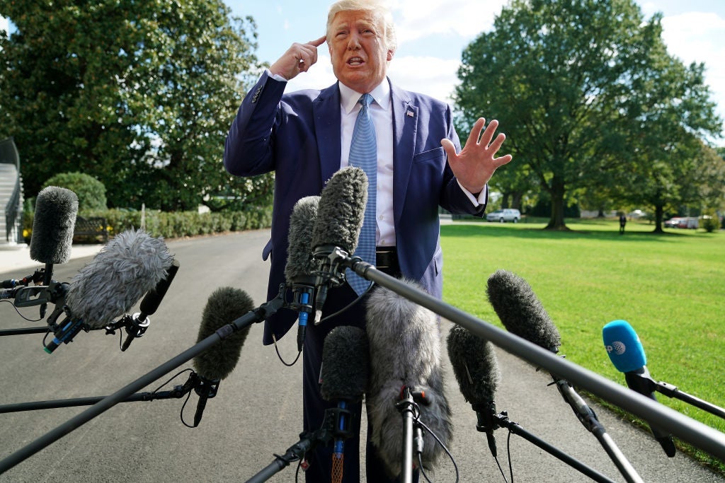 Trump points to his head while speaking into a group of microphones.
