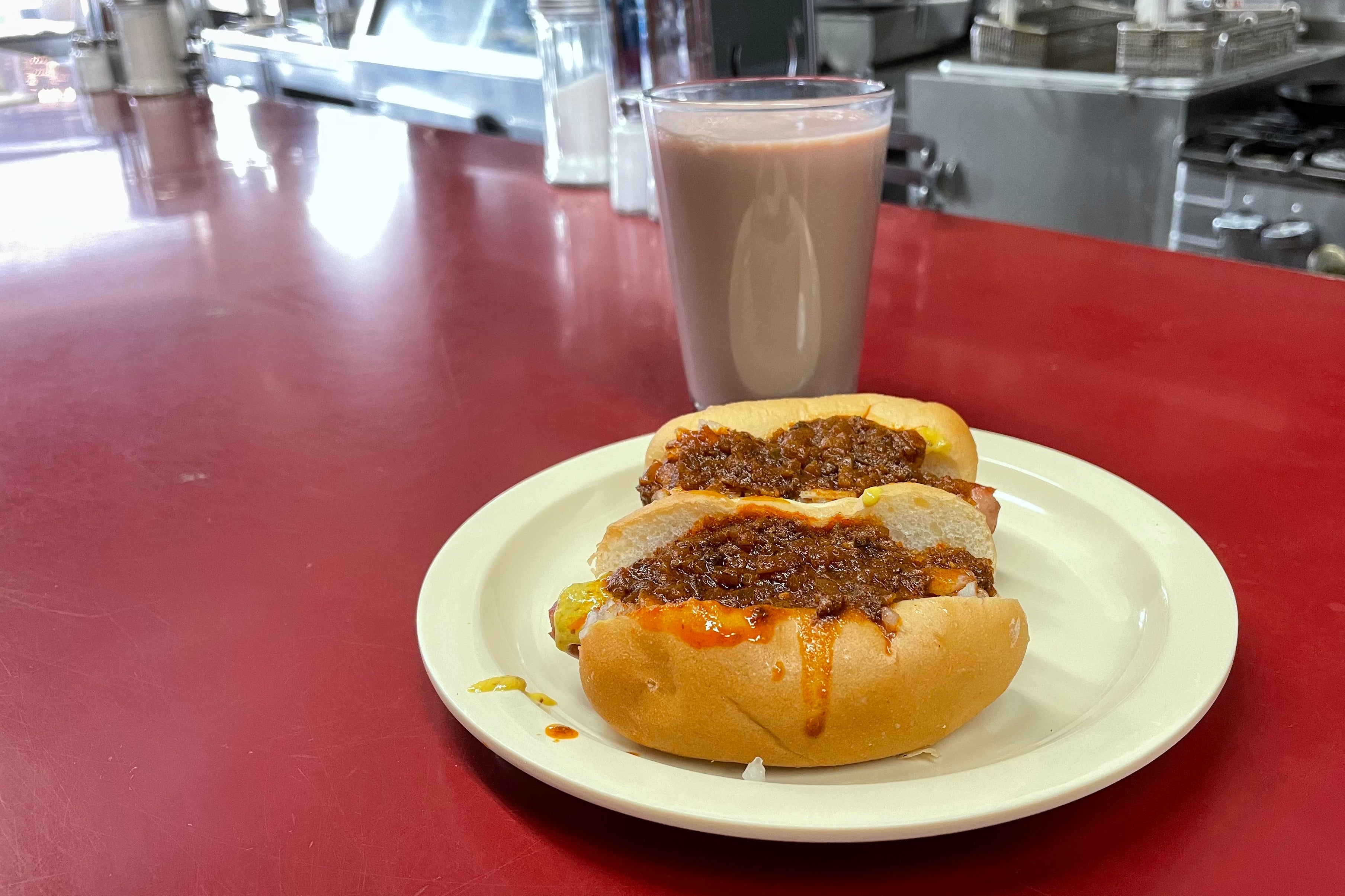Two mini chili dogs sit on a paper plate on a red counter.