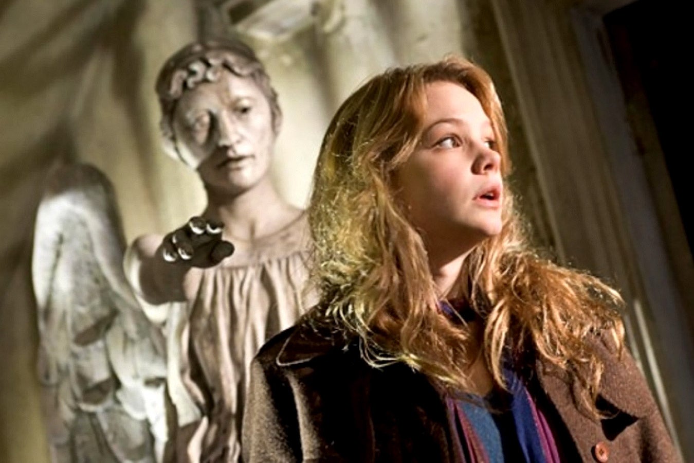 A blond woman looks off to the side, startled, while behind her, a statue reaches out to touch her.