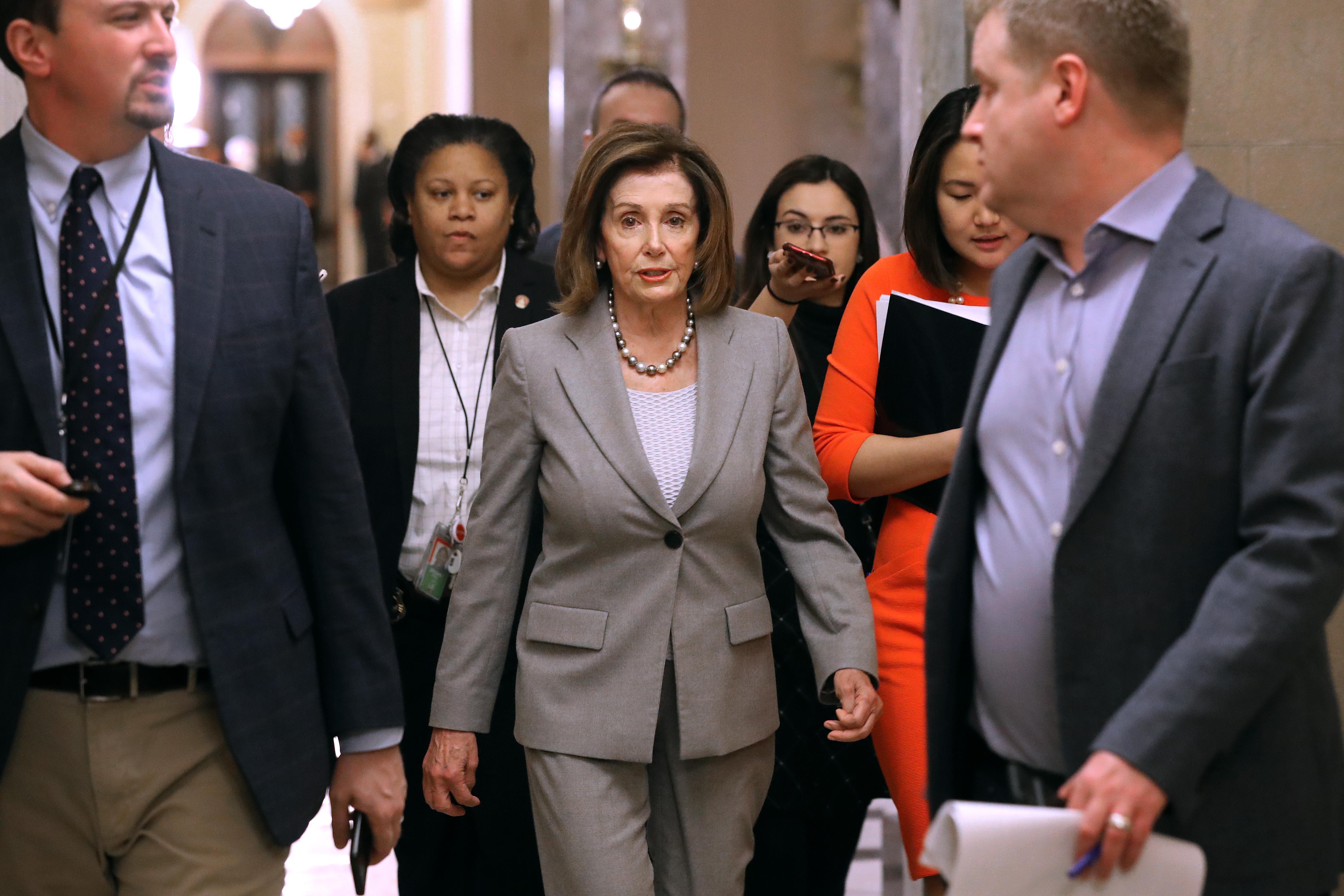 Speaker of the House Nancy Pelosi walks through the Capitol surrounded by people.