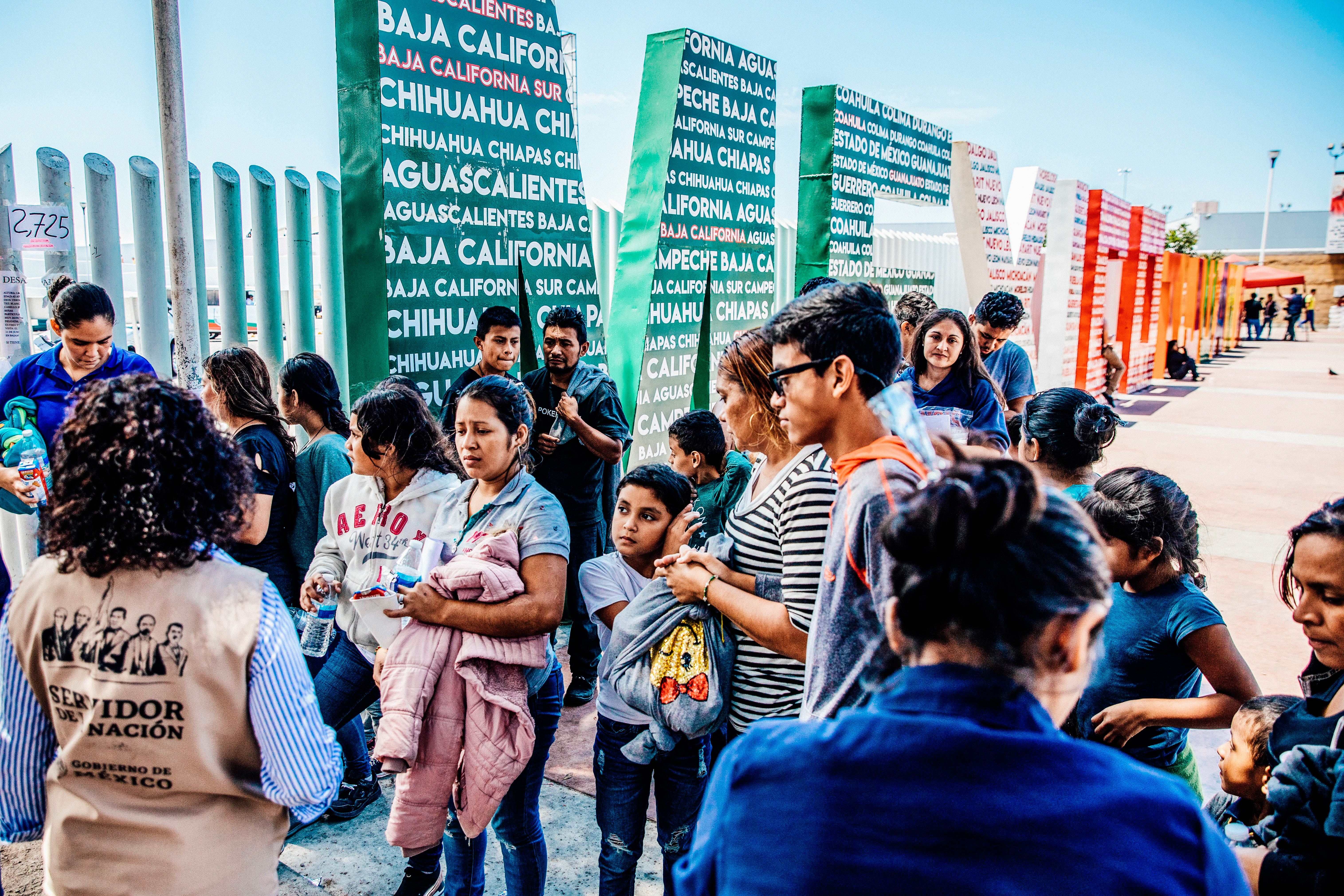 Central American migrants near a colorful sign that says MEXICO.